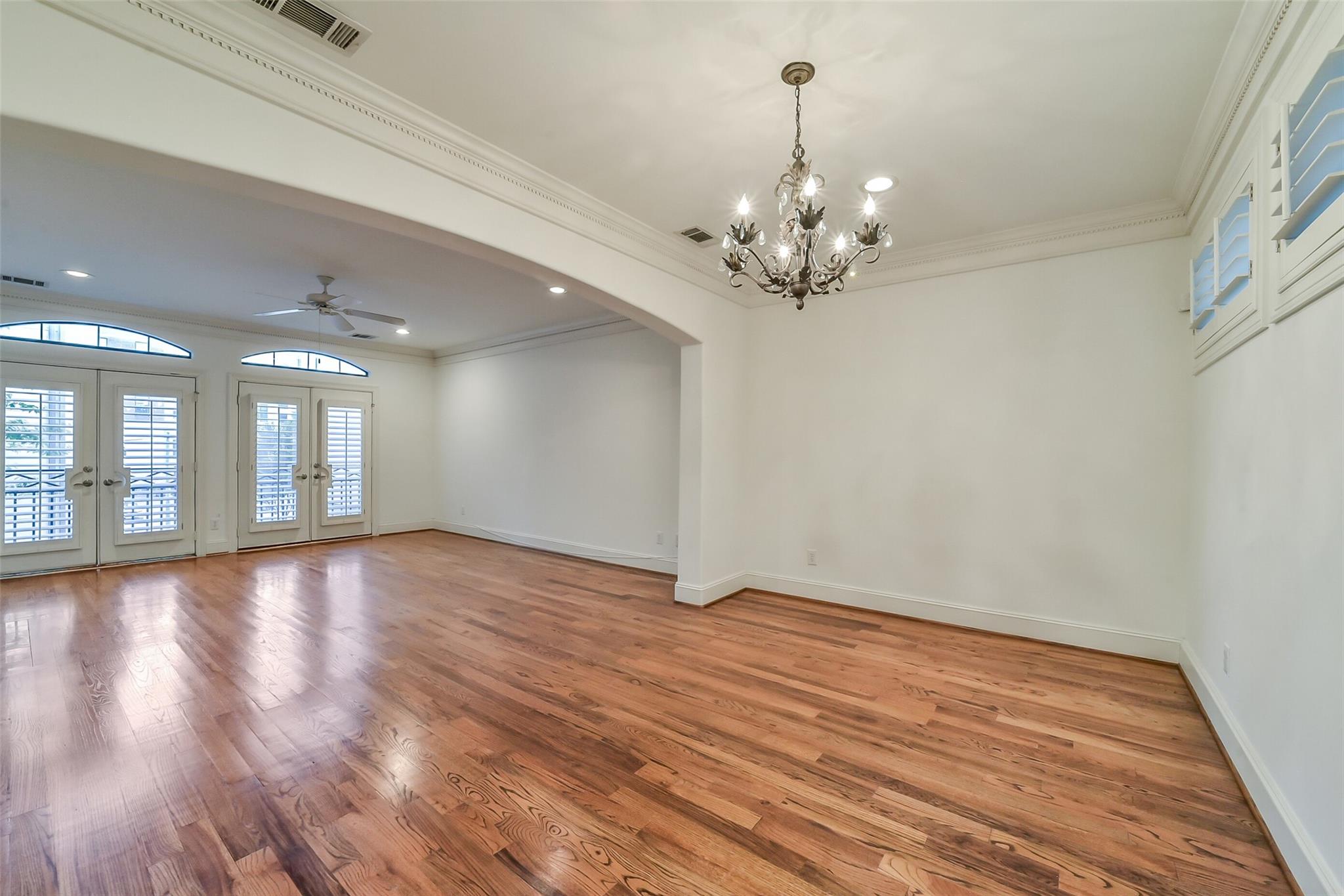 Empty living and dining room with hardwood floors, a chandelier, and shuttered French doors.
