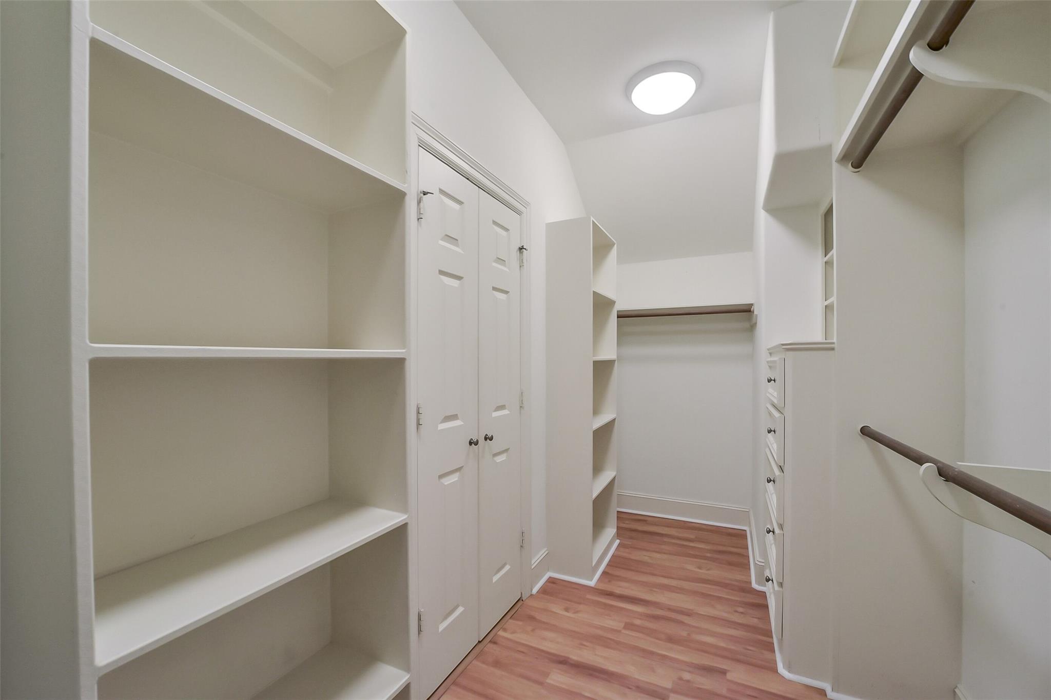 Walk-in closet with built-in shelving, hanging rods, drawers, and reddish wood flooring.