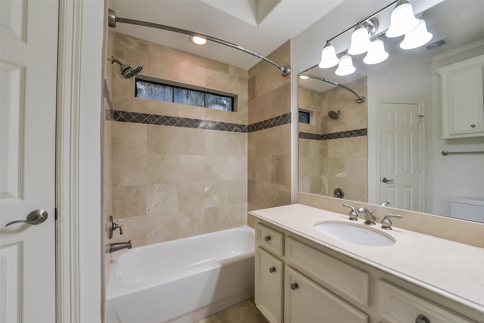 Bathroom with beige tiled bathtub surround, narrow window, and cream vanity with oval sink.