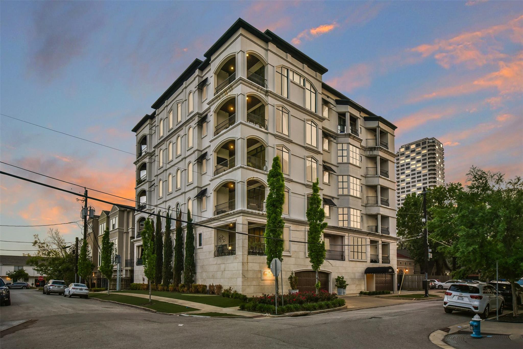 Multi-story condominium building with arched balconies and landscaped frontage at dusk.