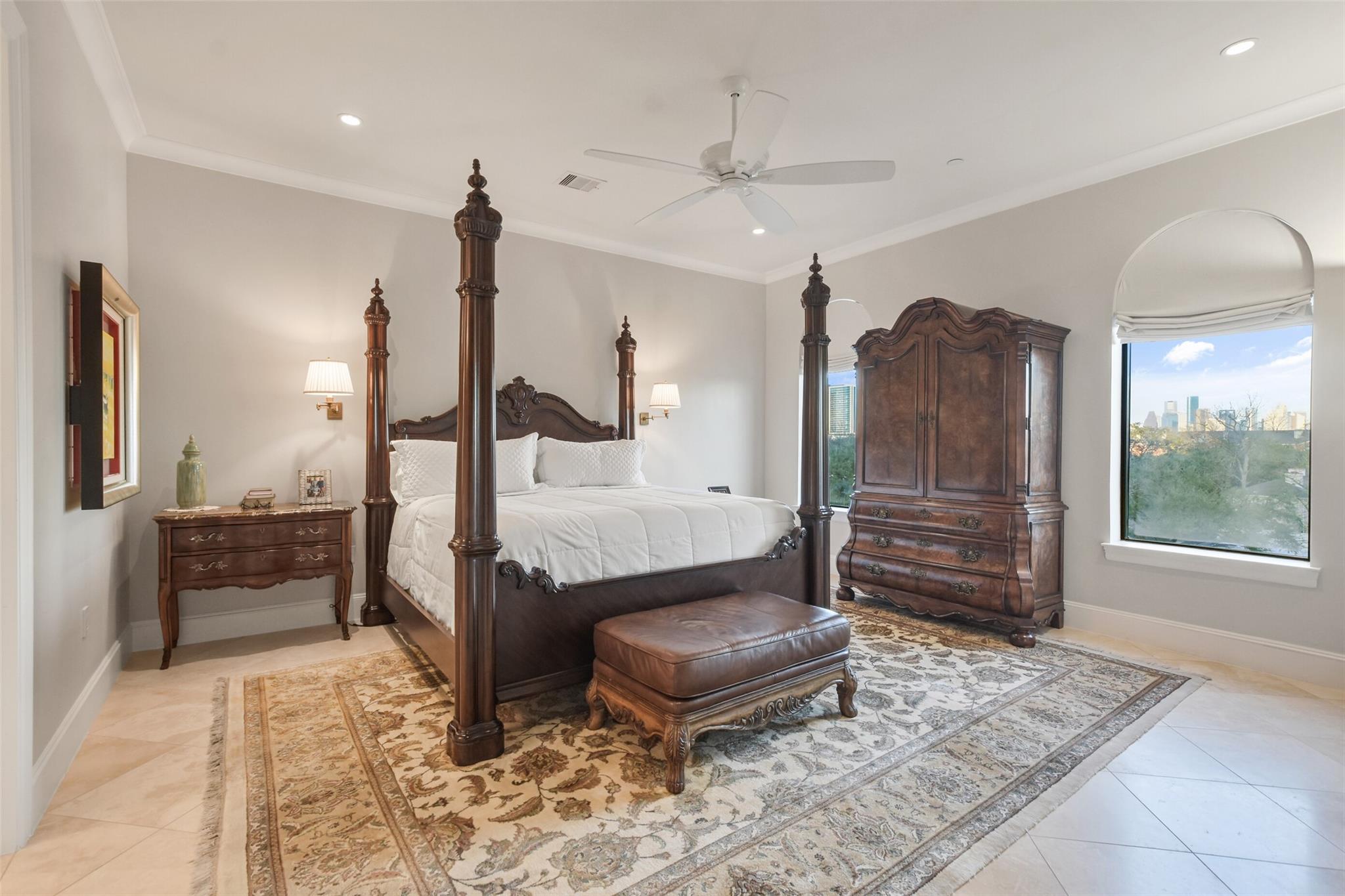 Furnished bedroom with a carved four-poster bed and arched window overlooking the Houston skyline.