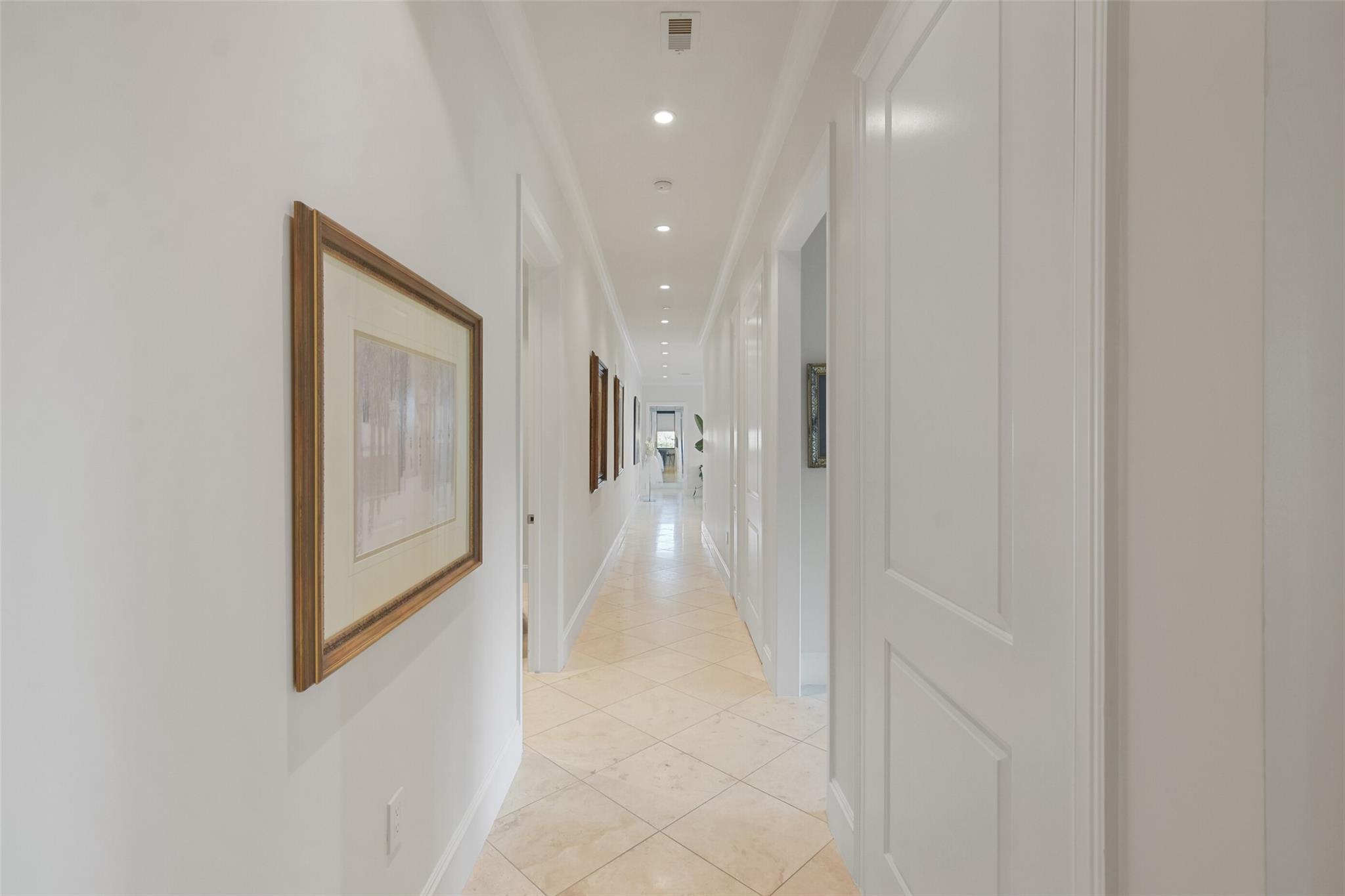 Bright tiled hallway with recessed lights, framed artwork, and white paneled doorways.