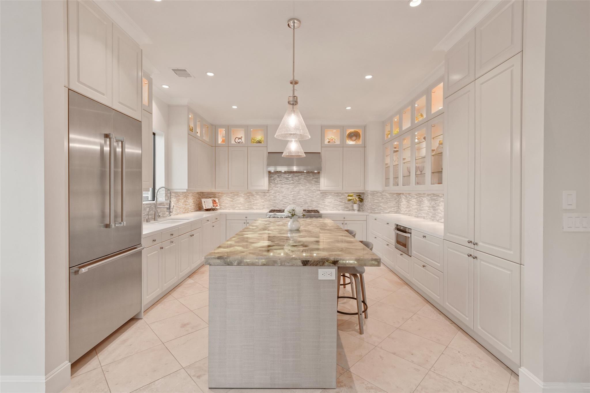 Bright kitchen with white cabinetry, stainless appliances, and a large stone island with stools.