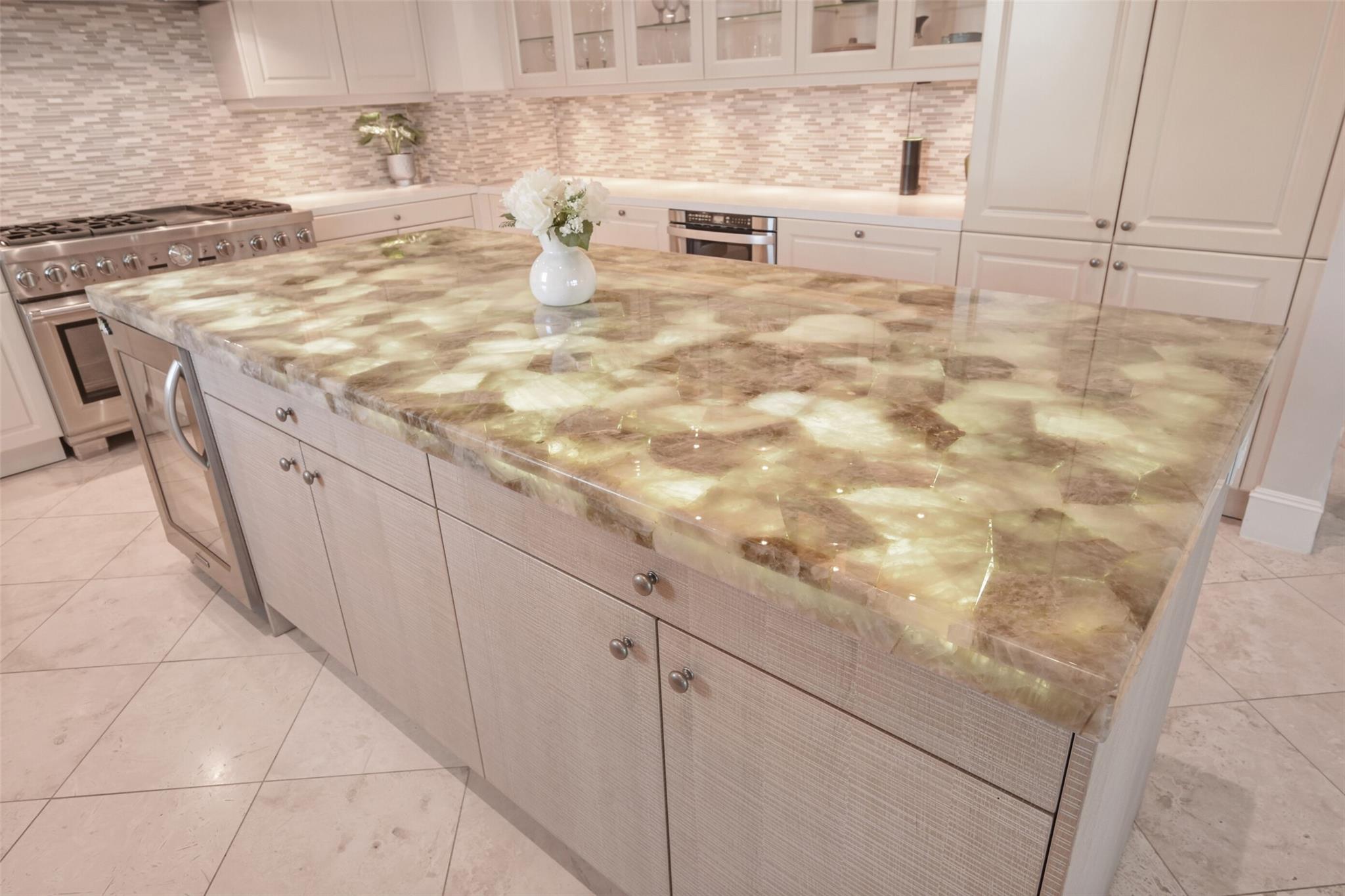 Kitchen with a large glowing stone island, white cabinetry, and stainless-steel range.
