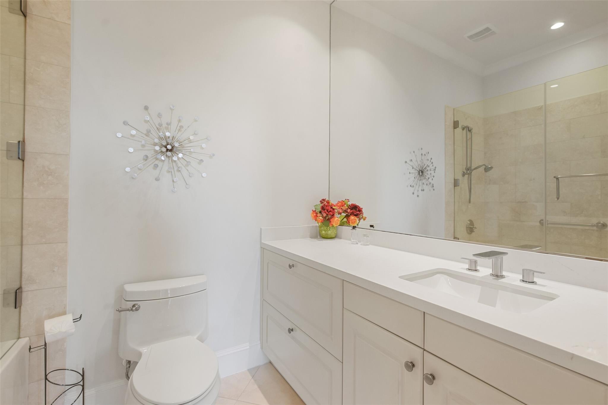 Bathroom with a long white vanity, large mirror, and glass-enclosed tiled shower.
