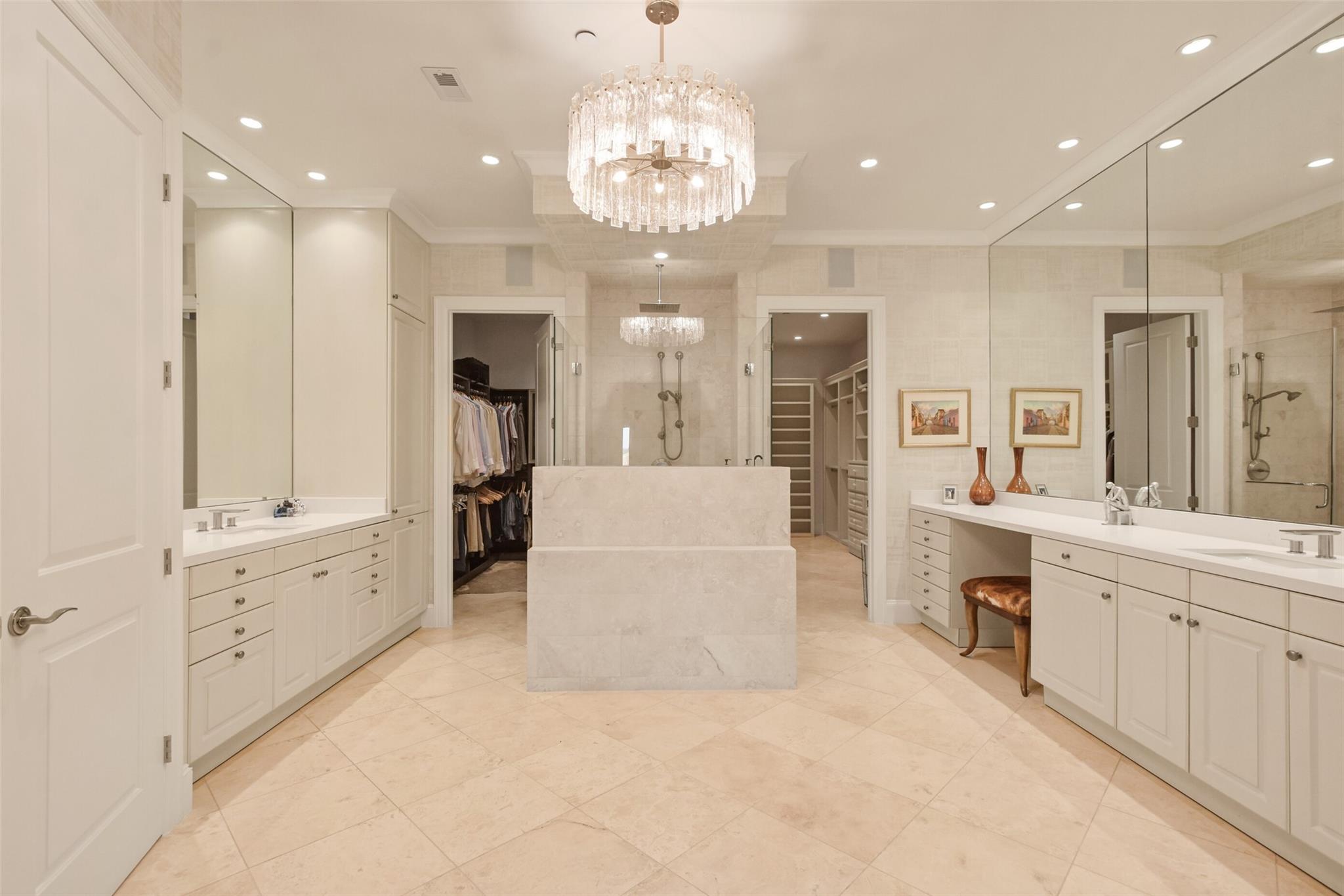 Spacious primary bathroom with a central soaking tub, crystal chandelier, double vanities, and walk-in closets.