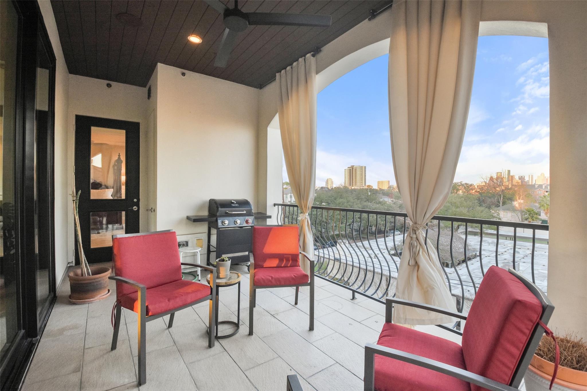 Furnished balcony with red chairs and a barbecue, overlooking trees and the Houston skyline.