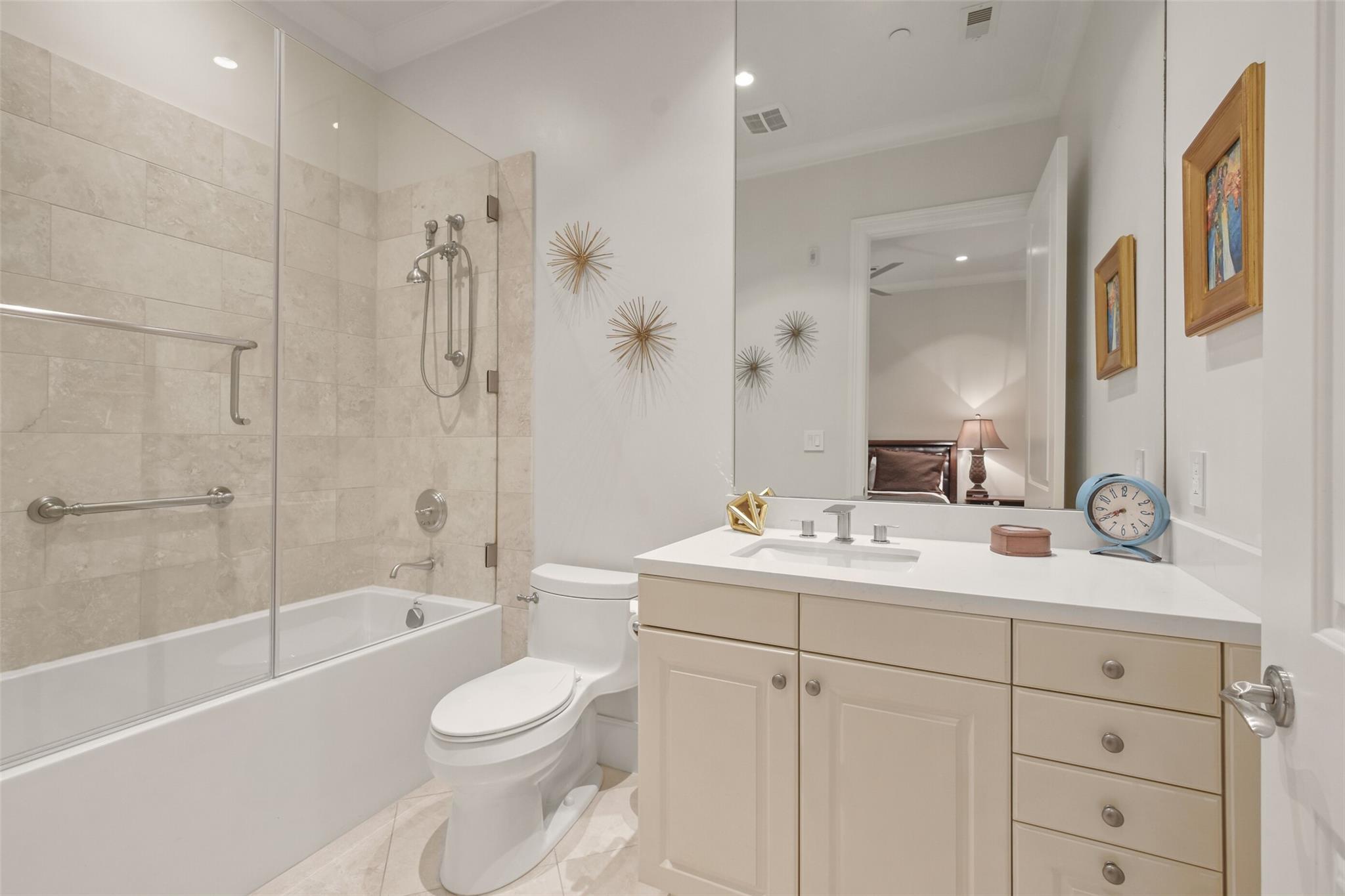 Bathroom with a glass-enclosed tub and shower, beige tile, and a wide vanity beneath a large mirror.