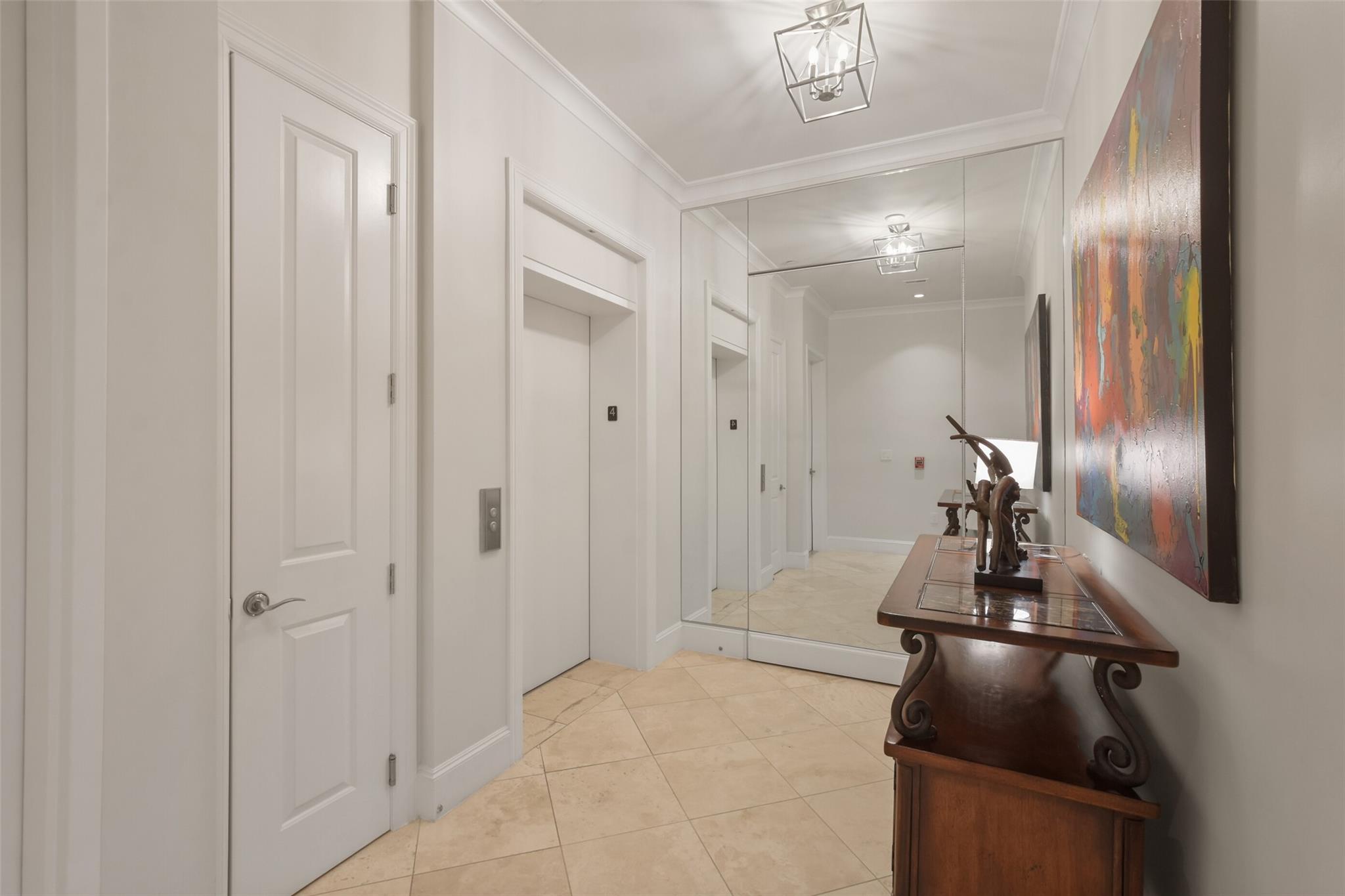 Condominium entry hall with mirrored doors, beige tile, and a wood console beneath colorful abstract art.