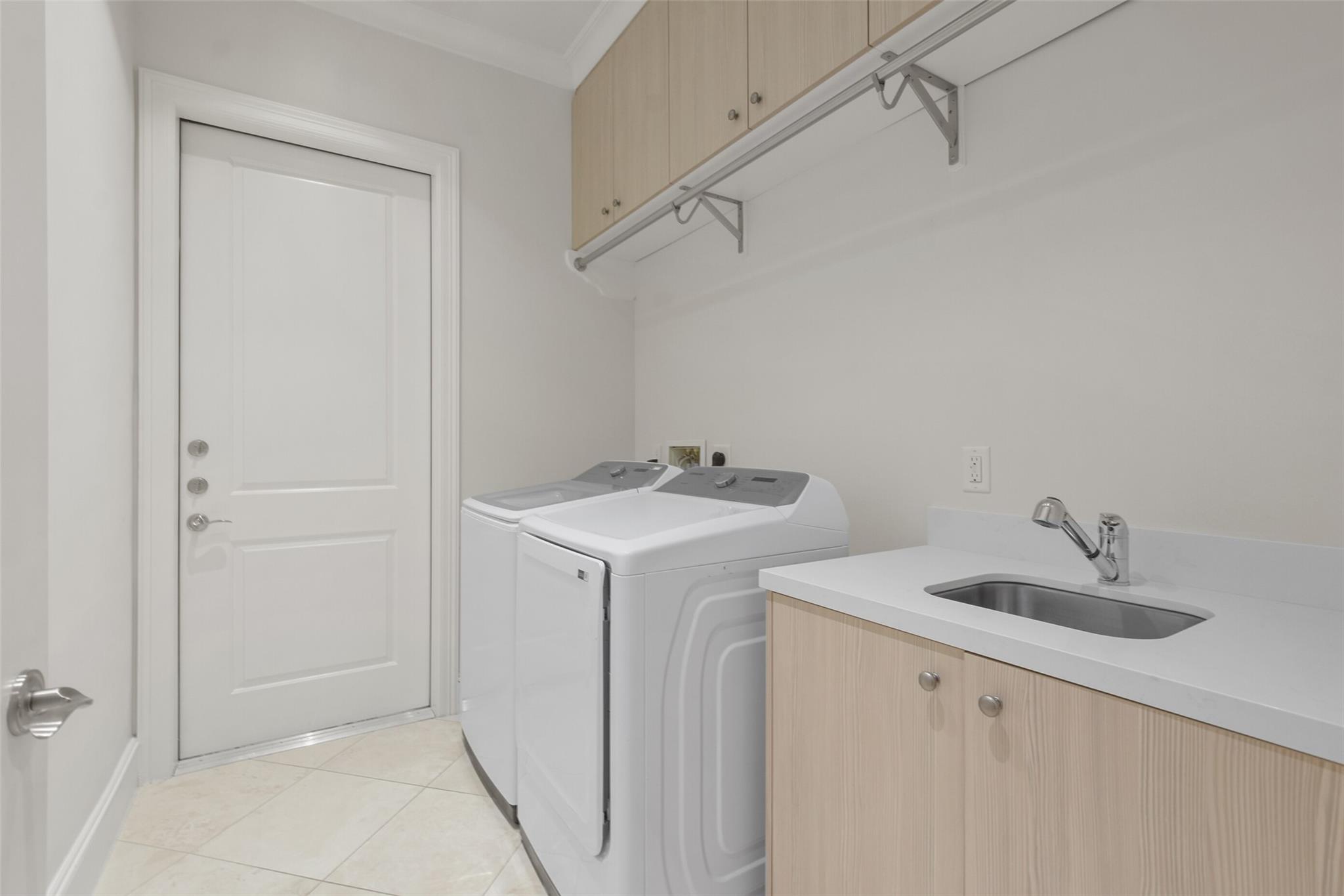 Laundry room with washer and dryer beside a utility sink and overhead cabinets.