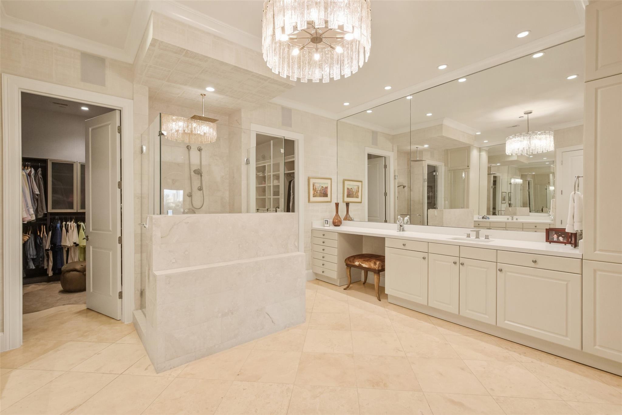 Marble bathroom with glass shower, double vanity, mirrored walls, and crystal chandelier.