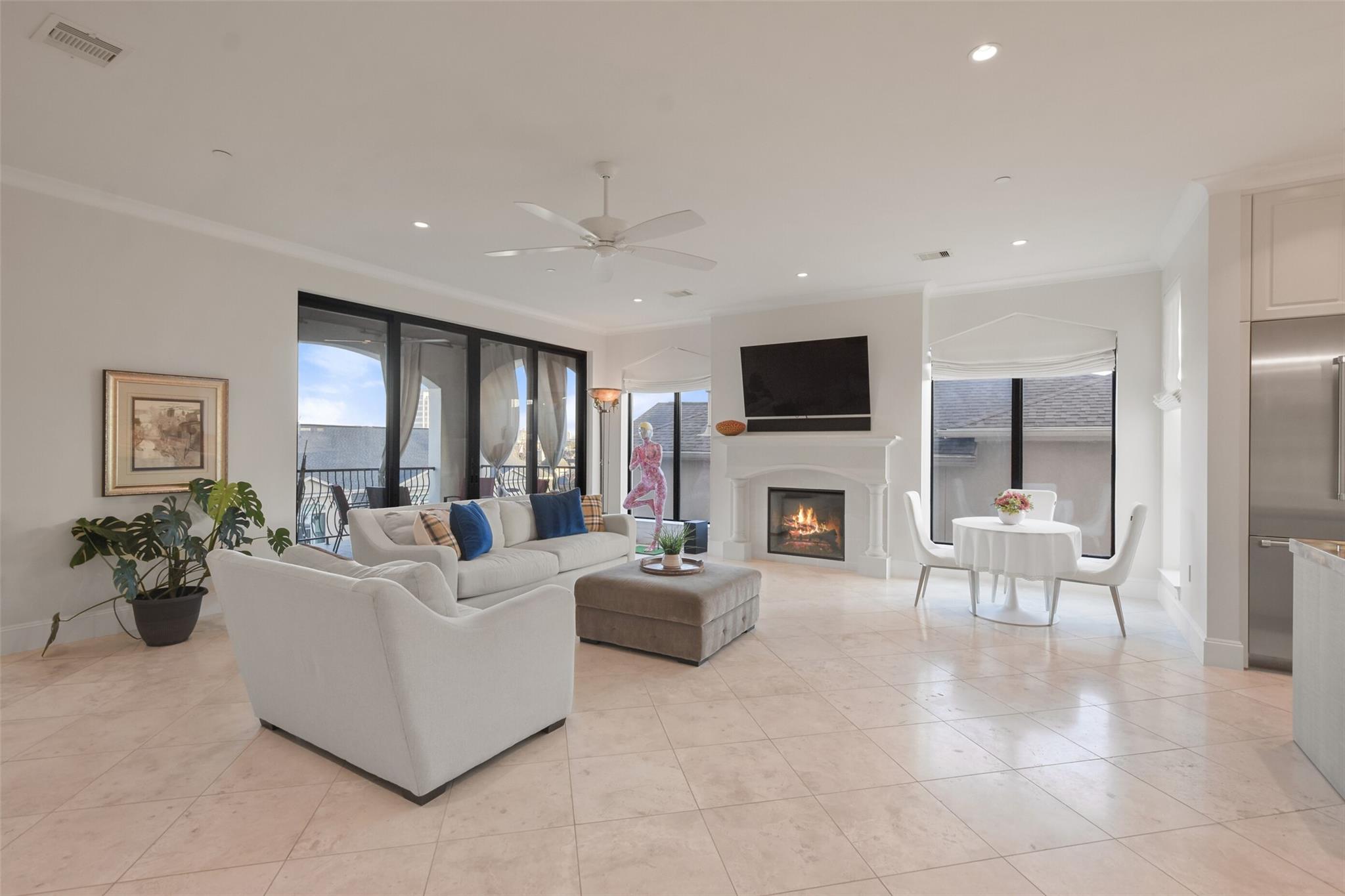 Staged living room with a fireplace, white seating, and large glass doors opening to a balcony.