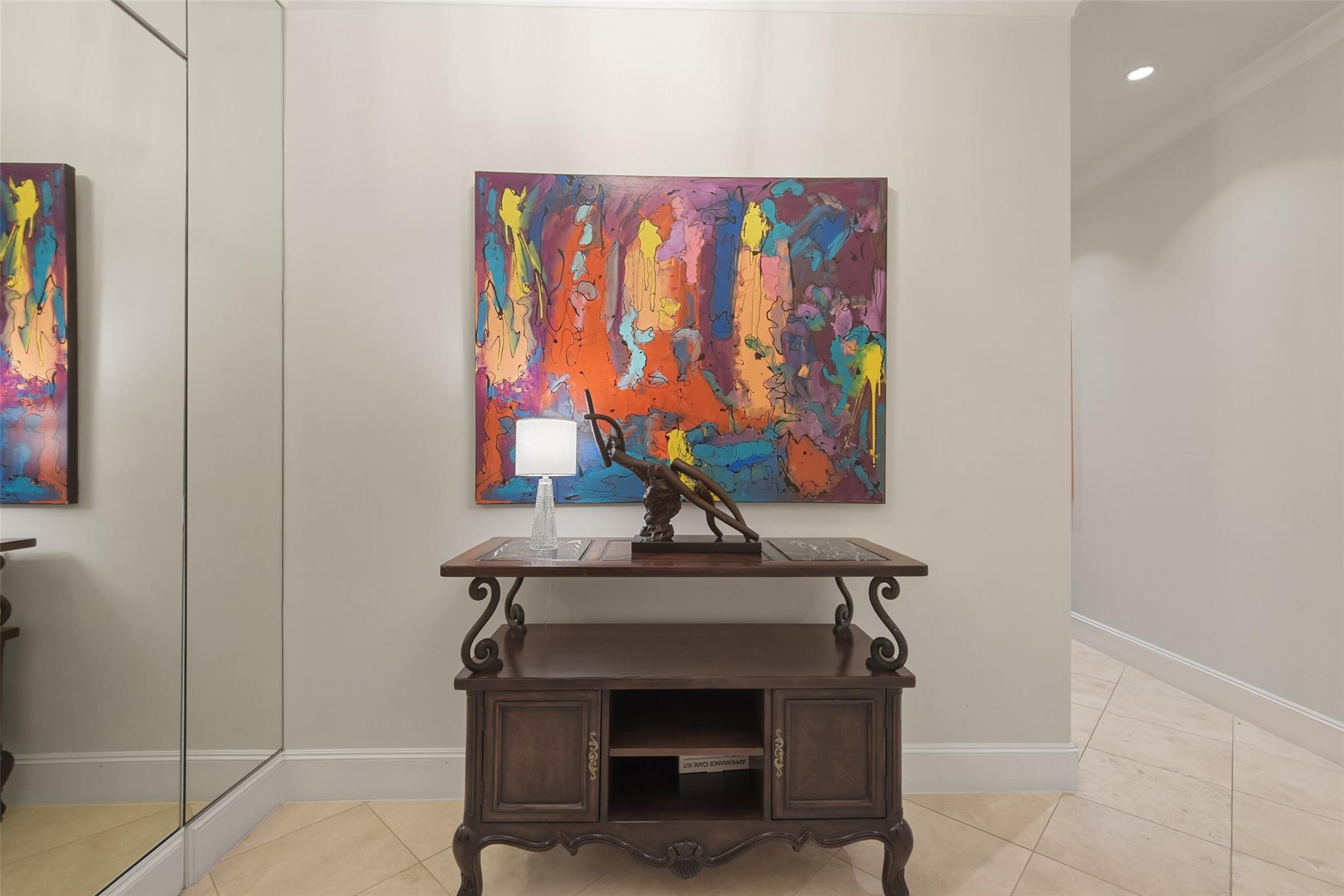 Condo entryway with a dark wood console beneath a vivid abstract painting and mirrored wall panels.