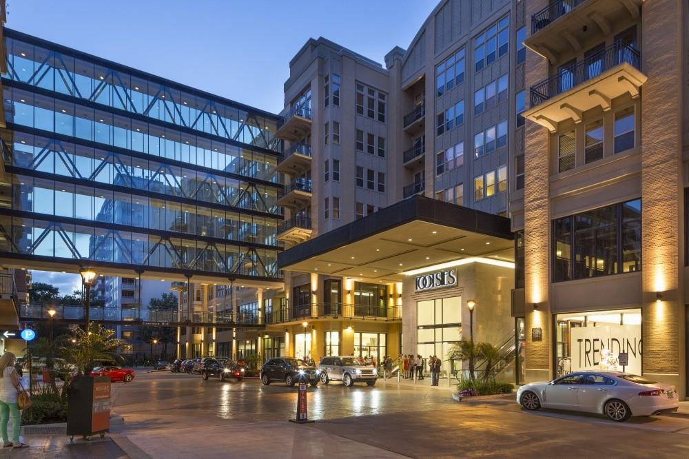 Urban building exterior at dusk with glass skybridges and illuminated storefronts.