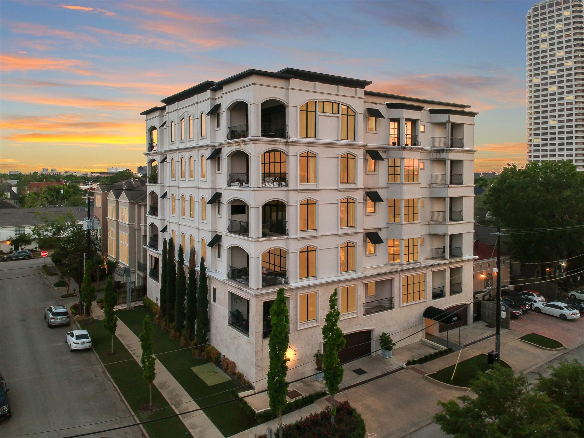 White condominium building with arched balconies and glowing windows at sunset, seen from above.