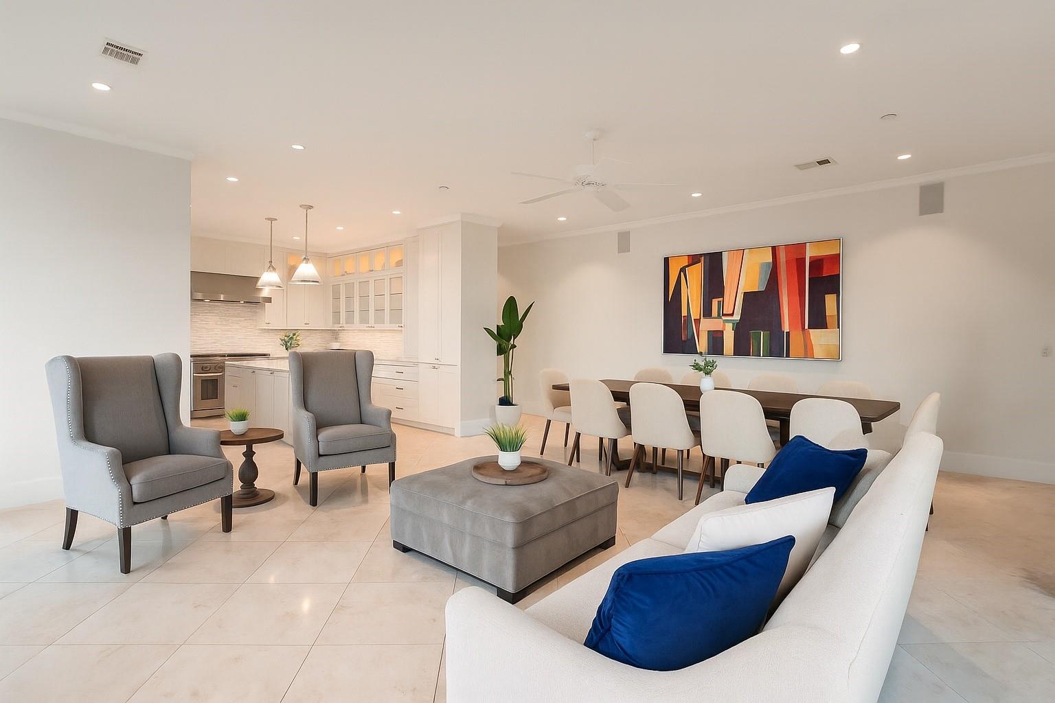 Open-plan living room with a white sofa, blue pillows, gray chairs, and a colorful abstract painting.