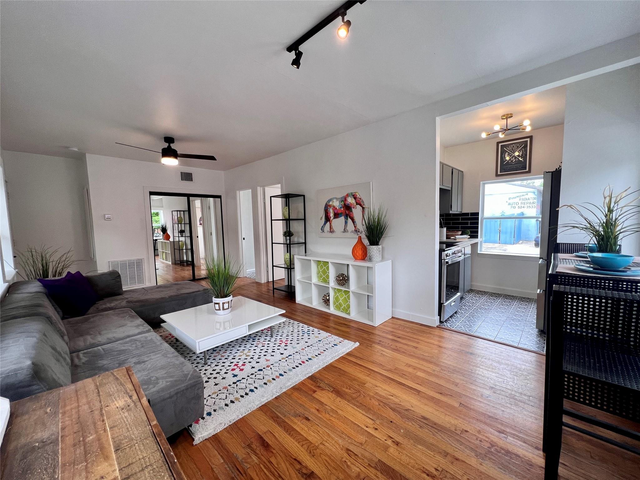 Open-plan living room and kitchen with a gray sectional, hardwood floors, and colorful elephant artwork.
