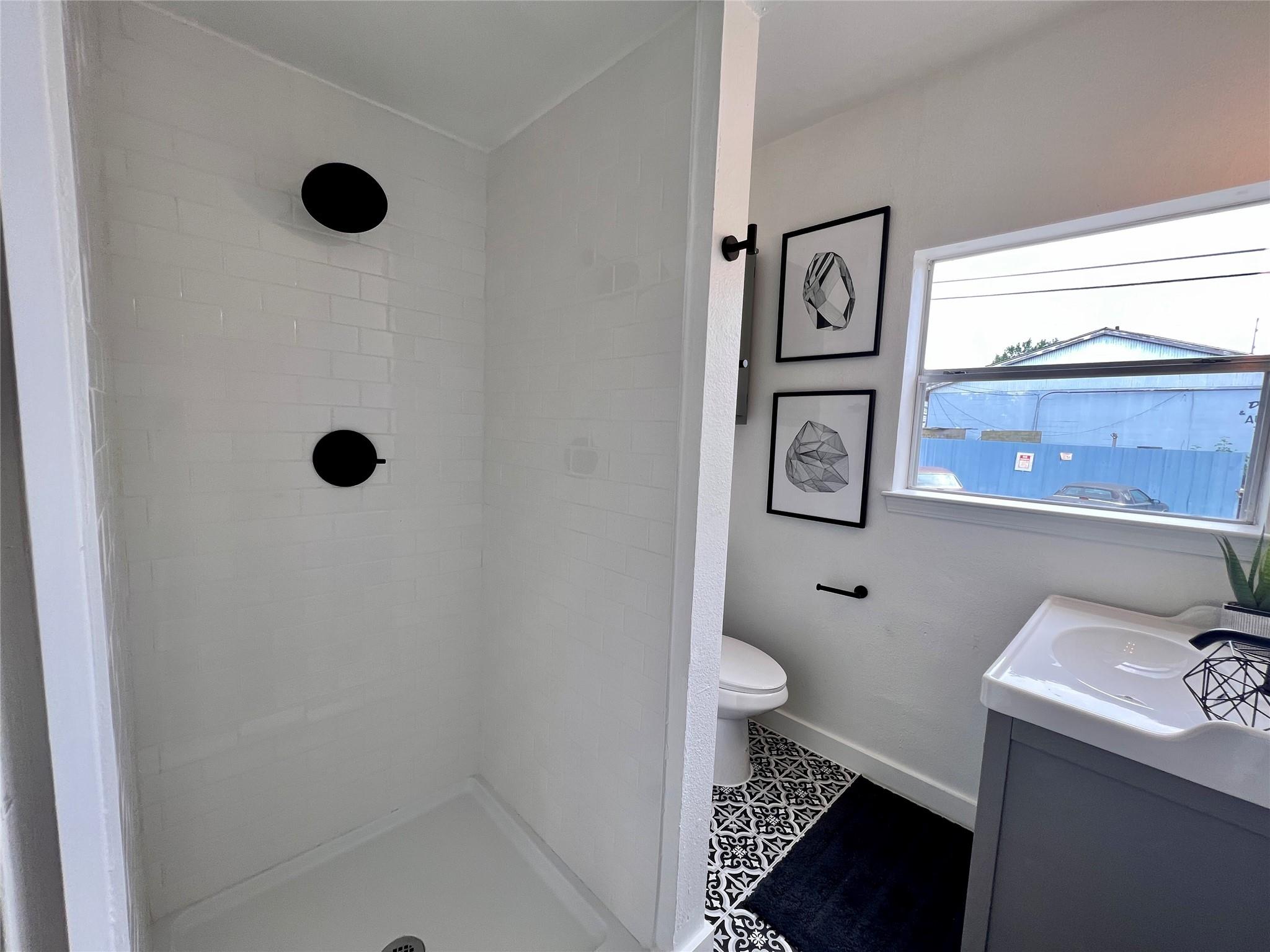 Bathroom with a white tiled walk-in shower, black fixtures, patterned floor, and gray vanity.