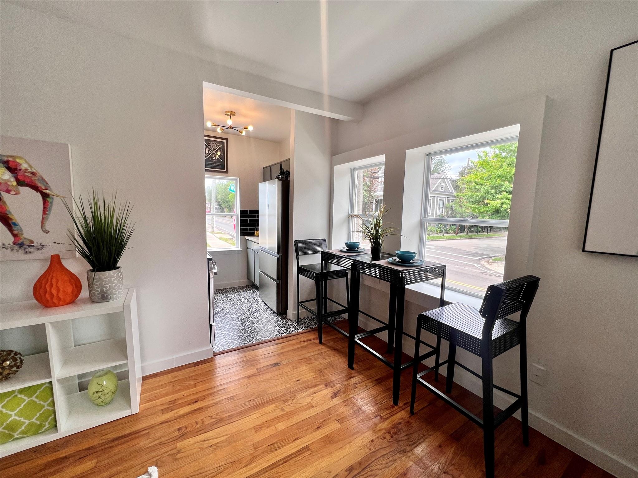 Dining area with a tall black table beside large windows, opening to a compact kitchen.