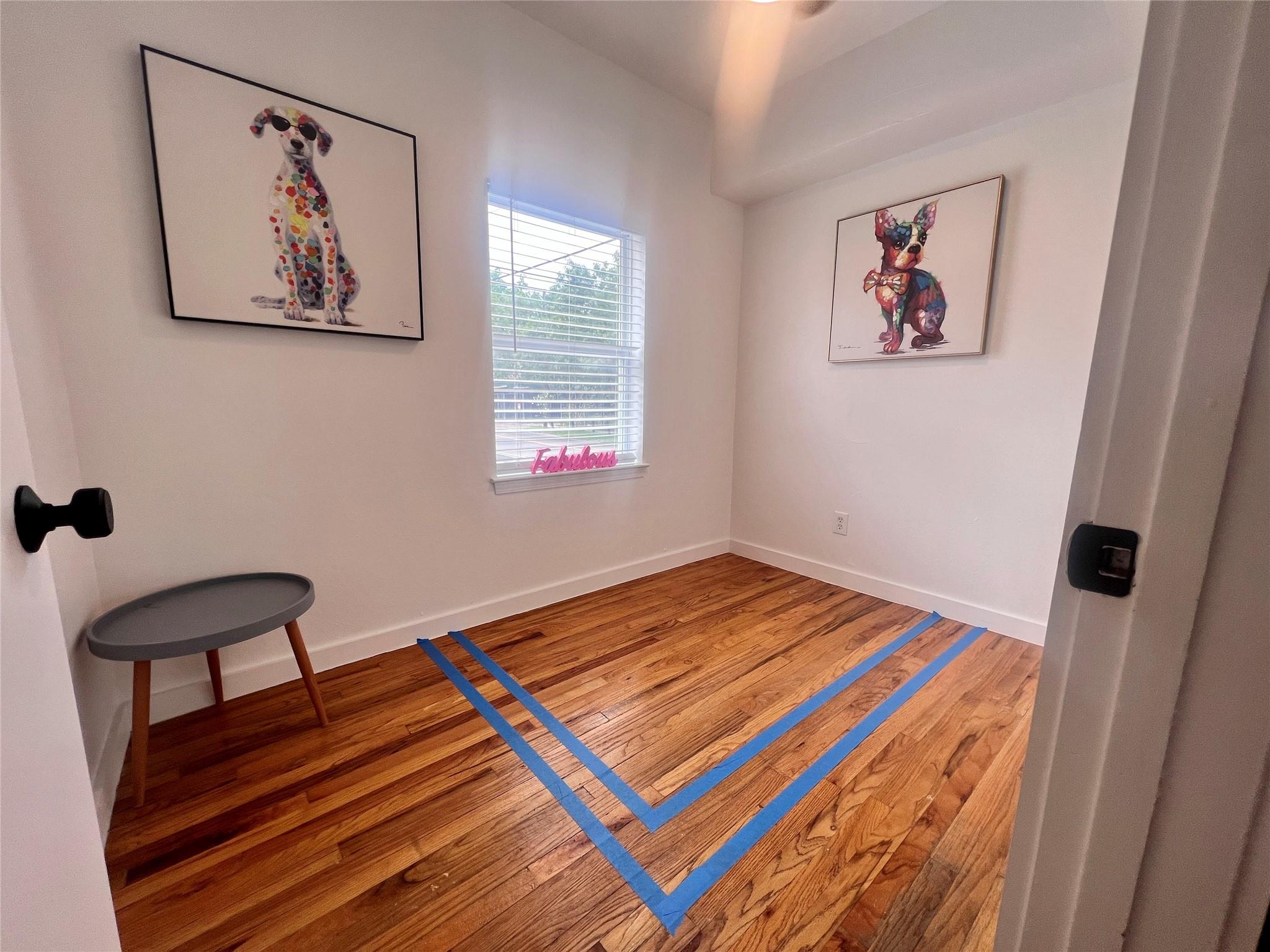 Small room with hardwood floors, blue tape markings, a window, and colorful dog artwork.