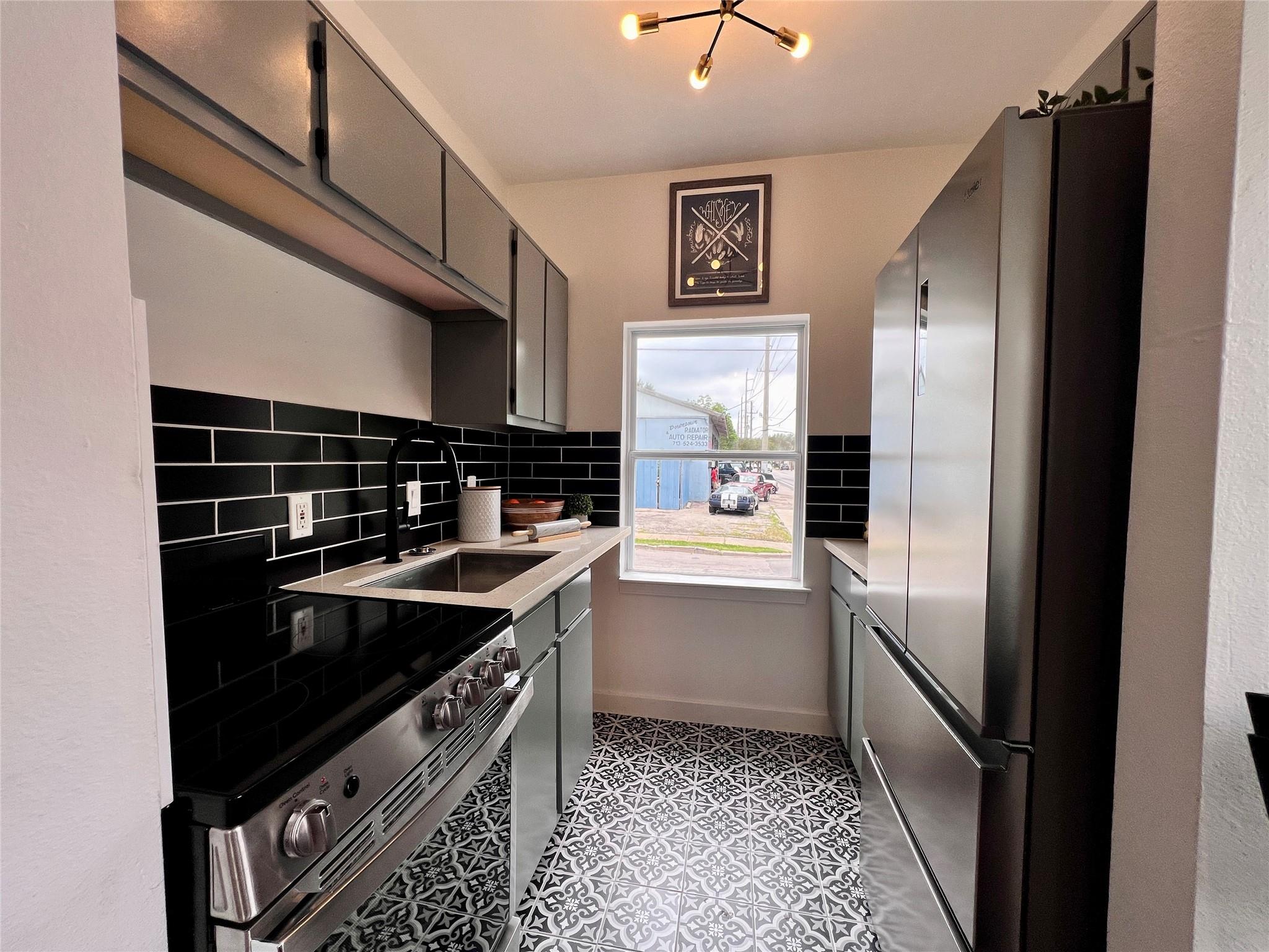 Narrow modern kitchen with black tile backsplash, stainless steel appliances, and patterned floor tiles.