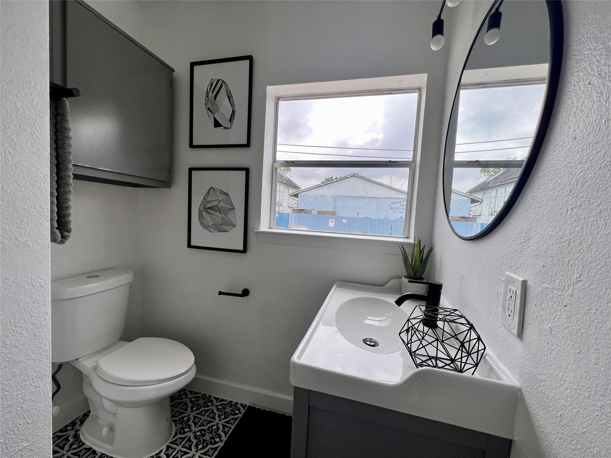 Bathroom with a white vanity, oval mirror, toilet, and patterned floor tile.