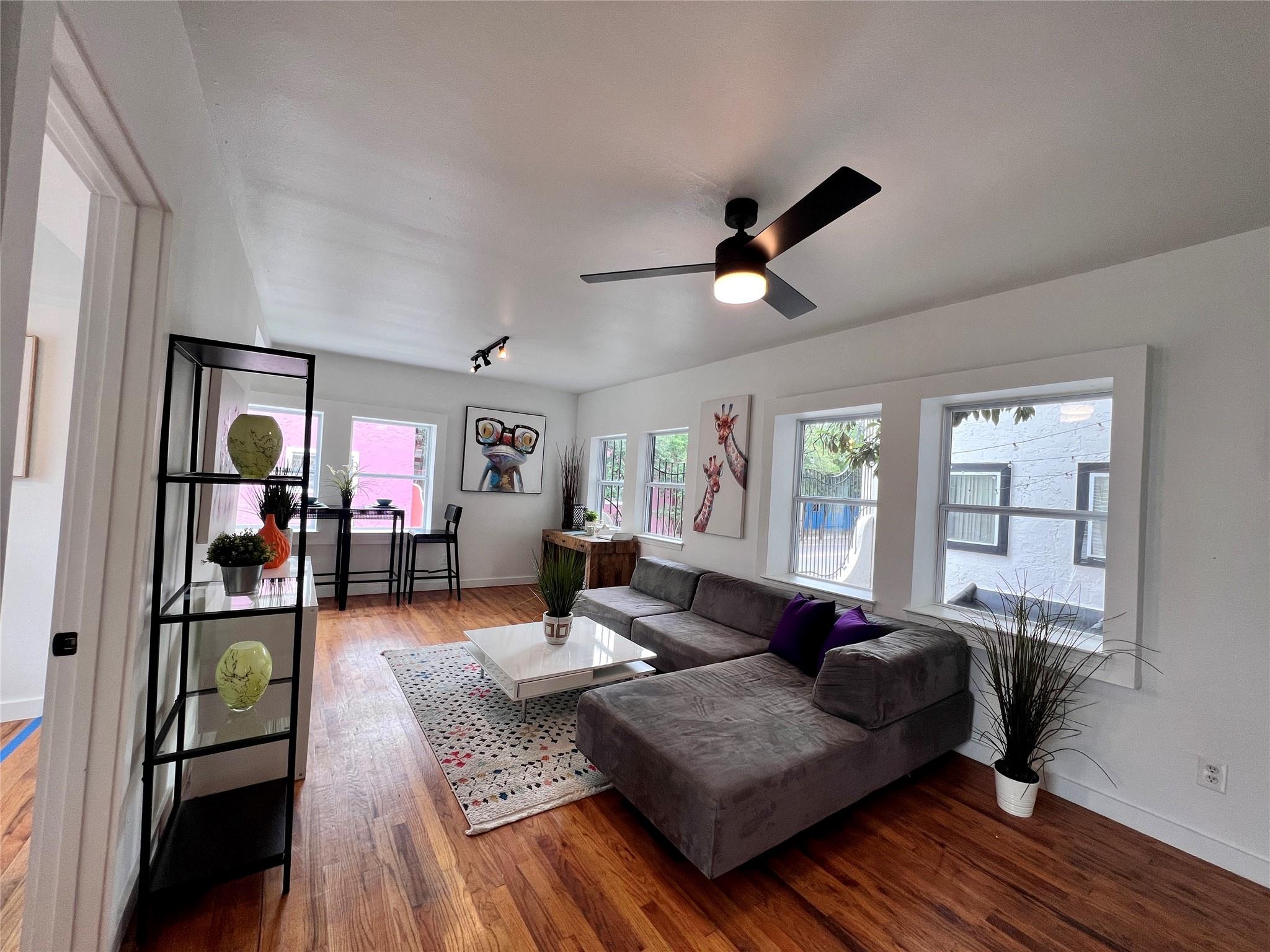 Living room with a gray sectional, white coffee table, hardwood floors, and large windows.