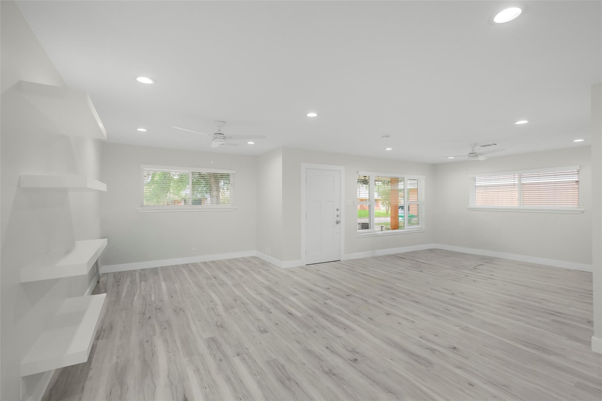 Vacant living room with gray plank flooring, built-in shelves, and windows beside the front door.