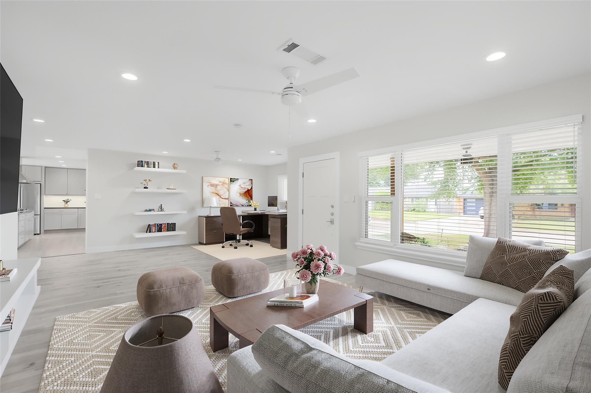Open-plan living room with a light-gray sectional, patterned rug, and wide windows overlooking the yard.