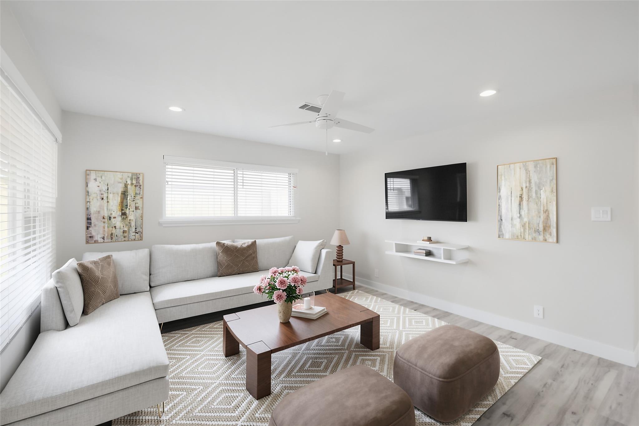 Staged living room with a gray sectional, wood coffee table, patterned rug, and wall-mounted television.