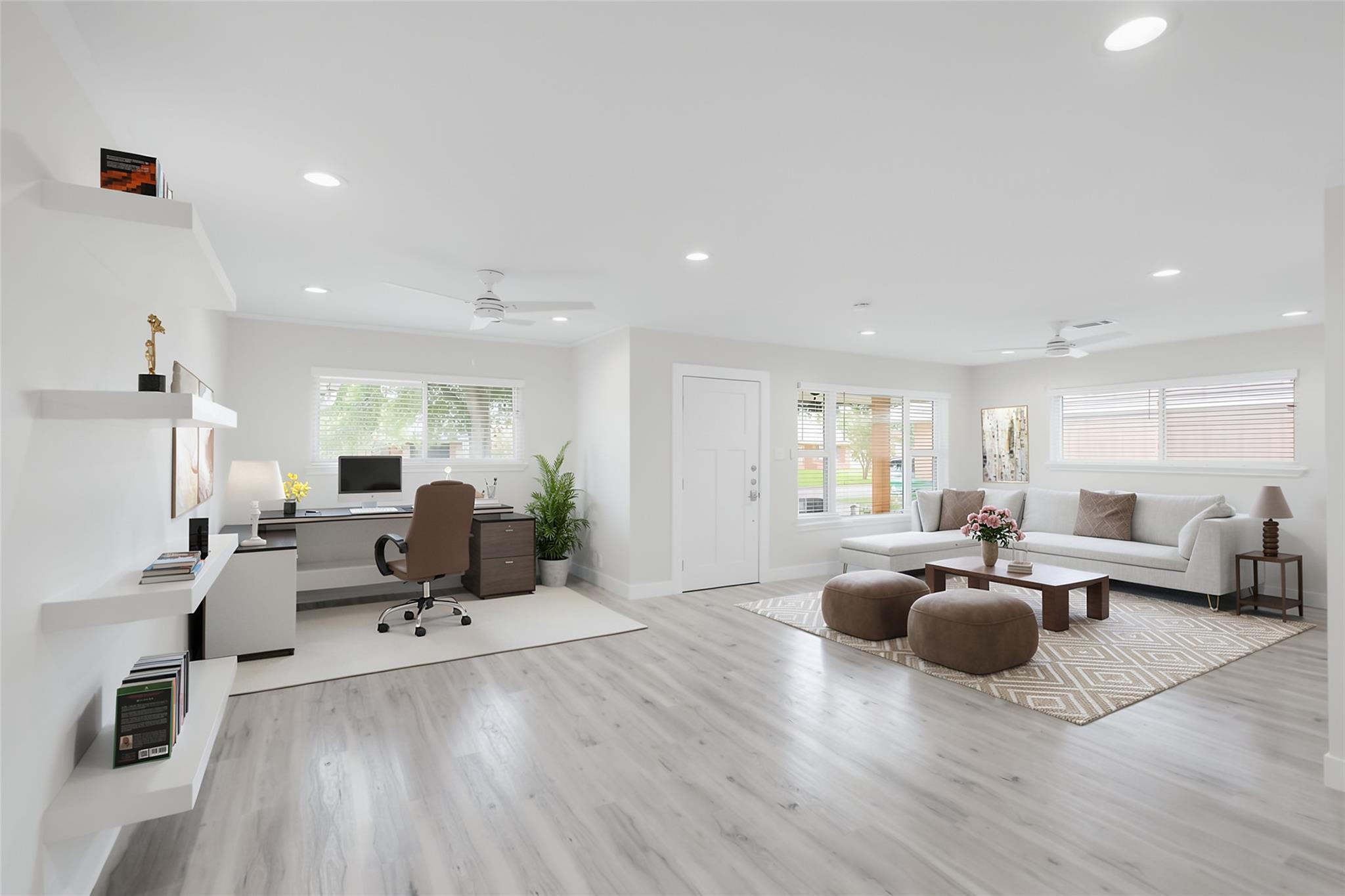 Open-plan living room and office with a white sectional, desk, and light wood floors.