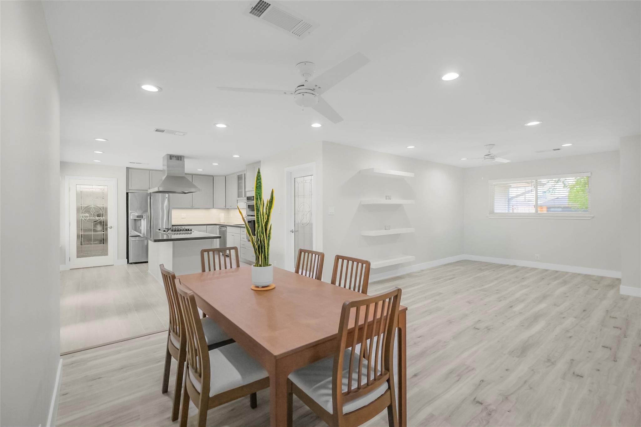 Open dining area and kitchen with a wooden table, stainless steel appliances, and light wood-look floors.