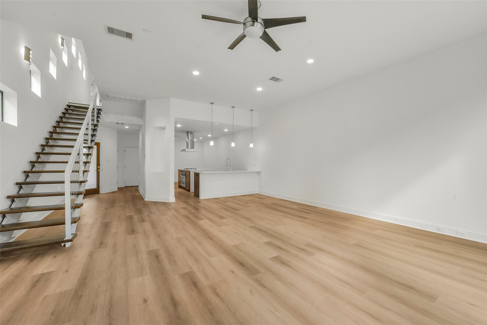Vacant open-plan living area with light wood floors, kitchen island, and open-riser staircase.