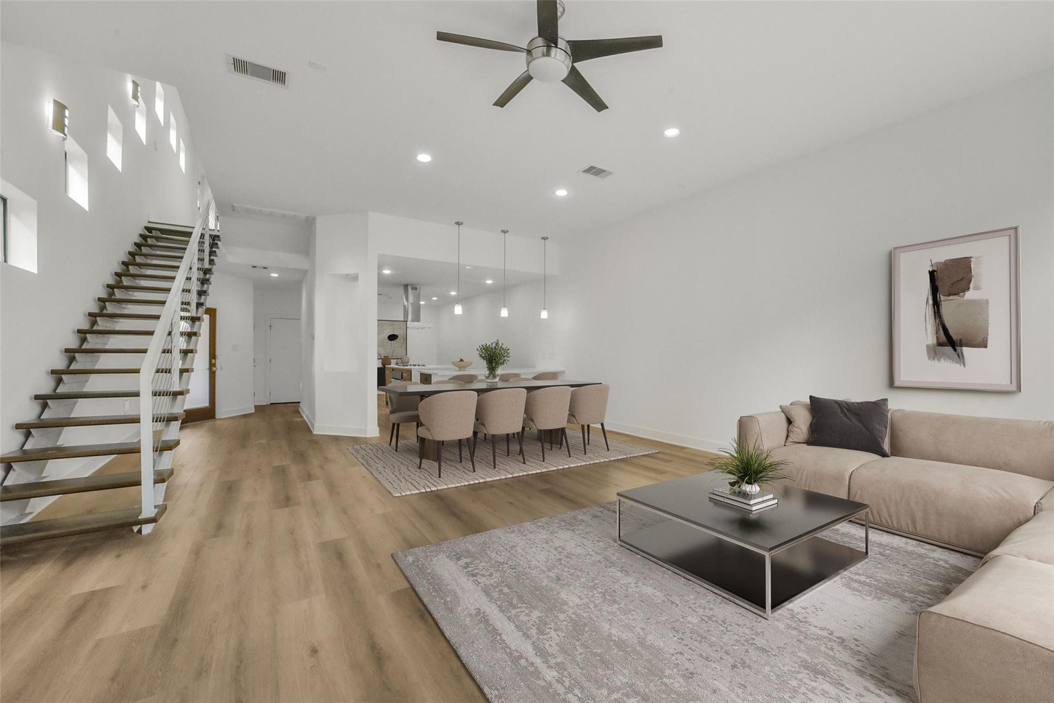 Open-plan living and dining room with a high ceiling, wood staircase, and beige sectional.