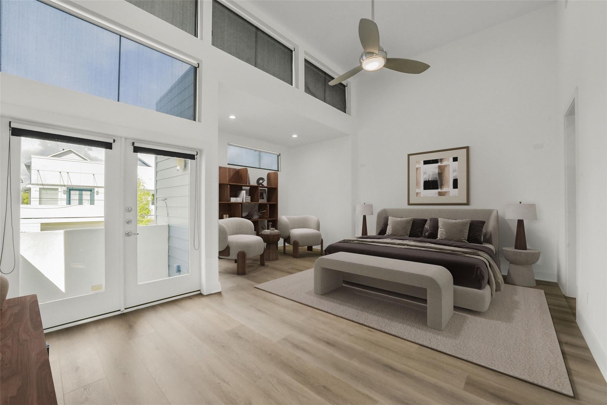 Staged bedroom with a king bed, lounge chairs, tall windows, and a ceiling fan.