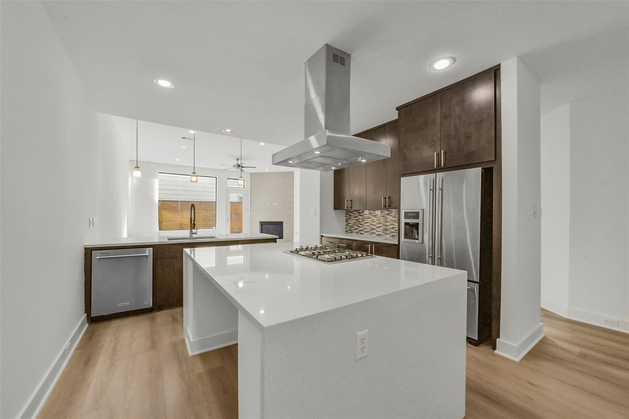 Modern kitchen with a large white island, gas cooktop, dark cabinets, and stainless steel appliances.