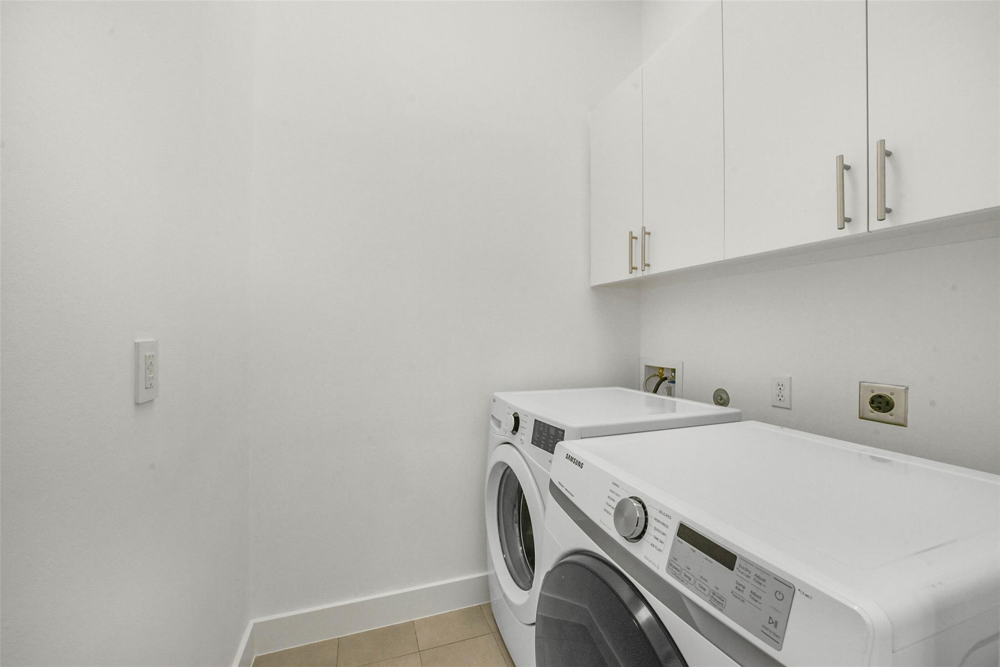 Laundry room with a front-loading washer and dryer beneath white cabinets.