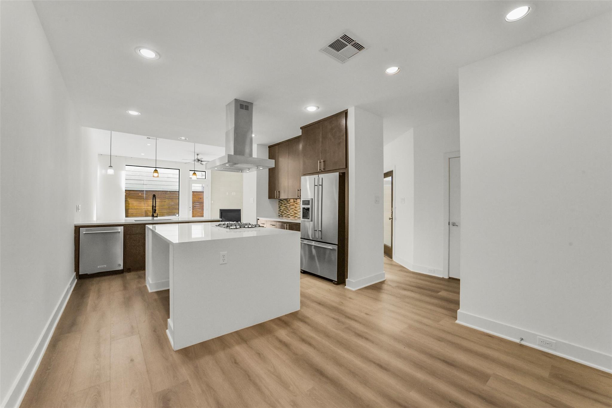 Modern kitchen with a large white island, dark wood cabinets, and stainless-steel appliances.