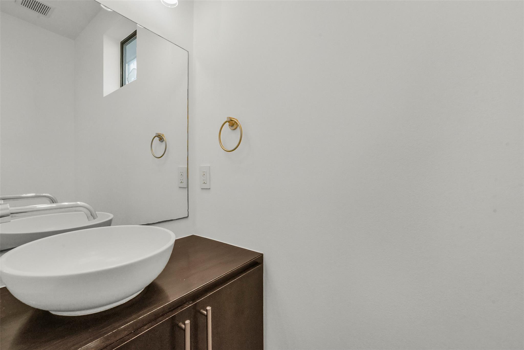 Bathroom vanity with a white vessel sink, dark wood cabinet, and brass towel ring.
