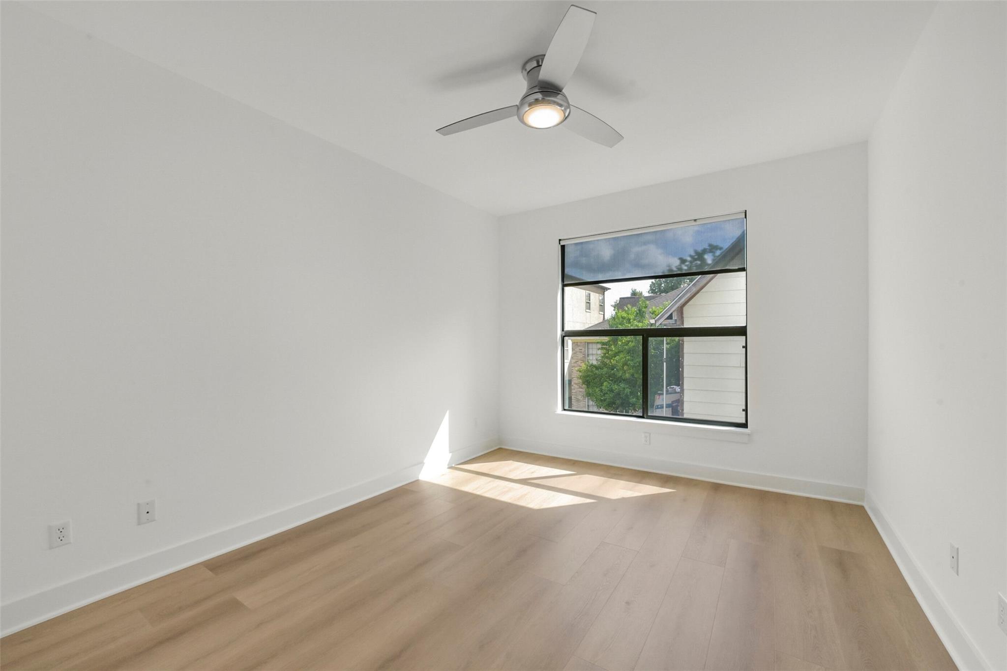 Empty bedroom with pale wood floors, a ceiling fan, and a large window.