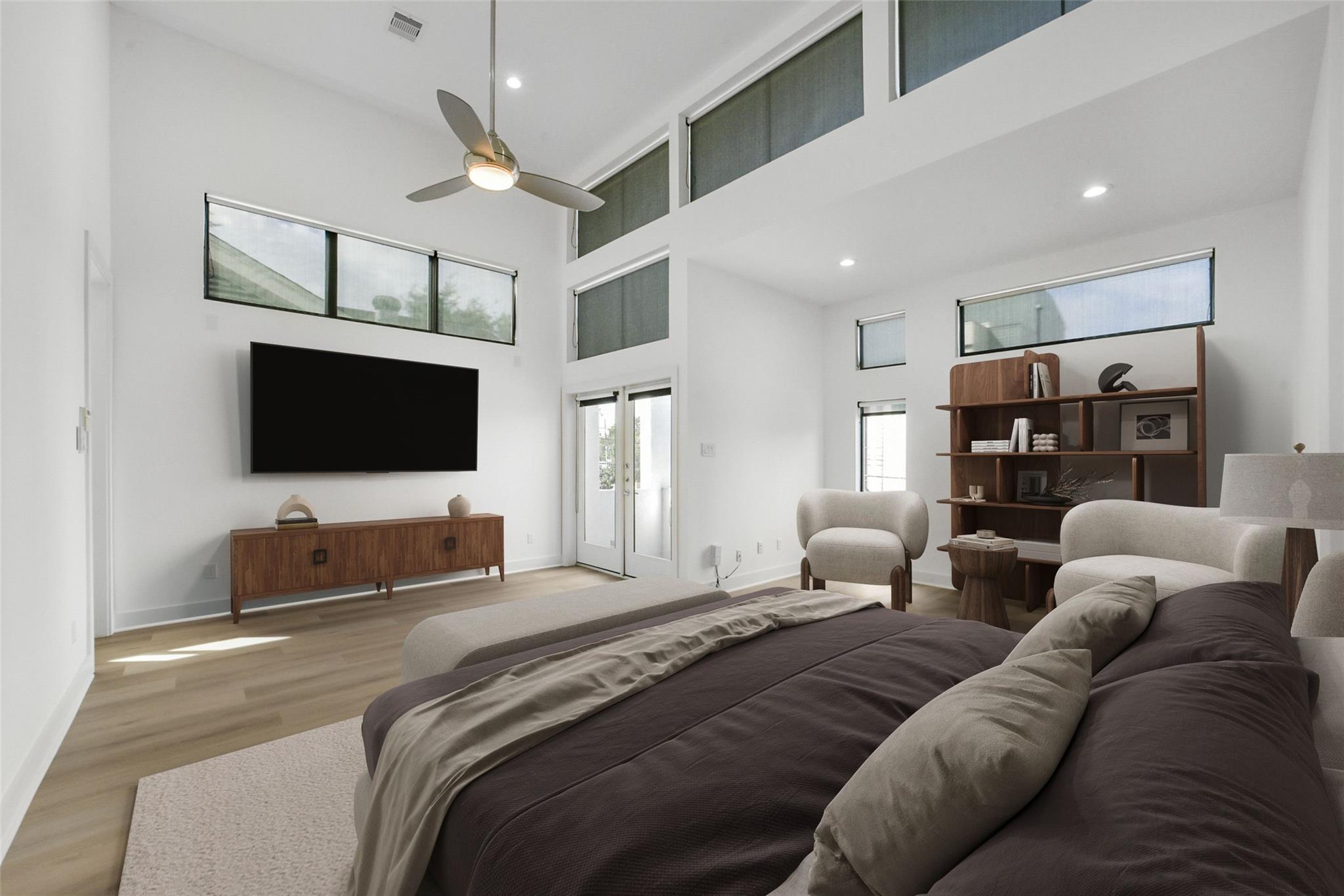 Staged bedroom with a tall ceiling, clerestory windows, ceiling fan, and sitting area.