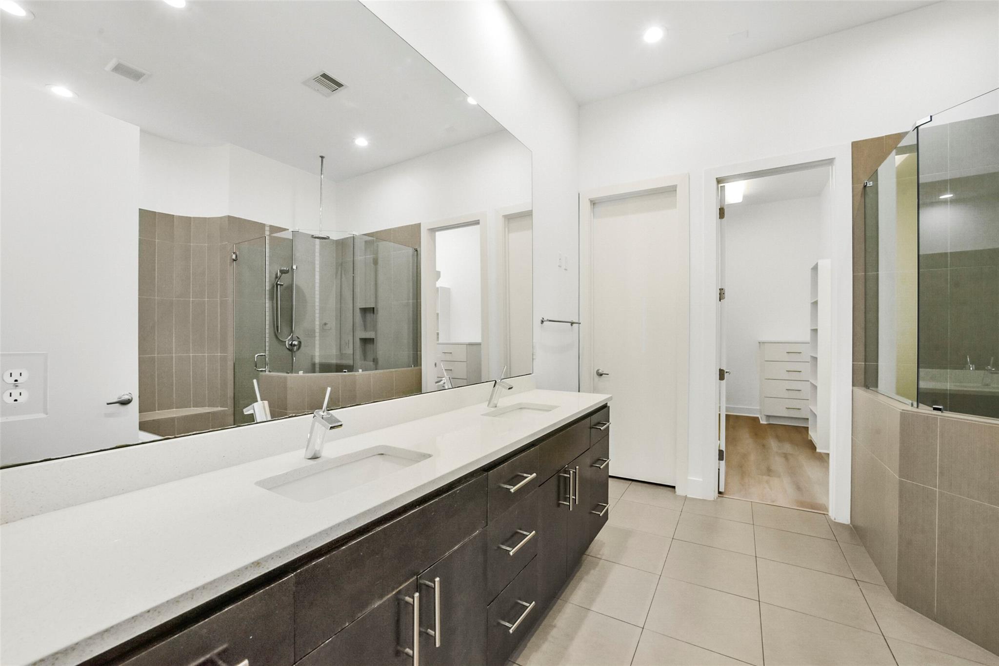 Modern bathroom with a long double vanity and glass-enclosed tiled shower.