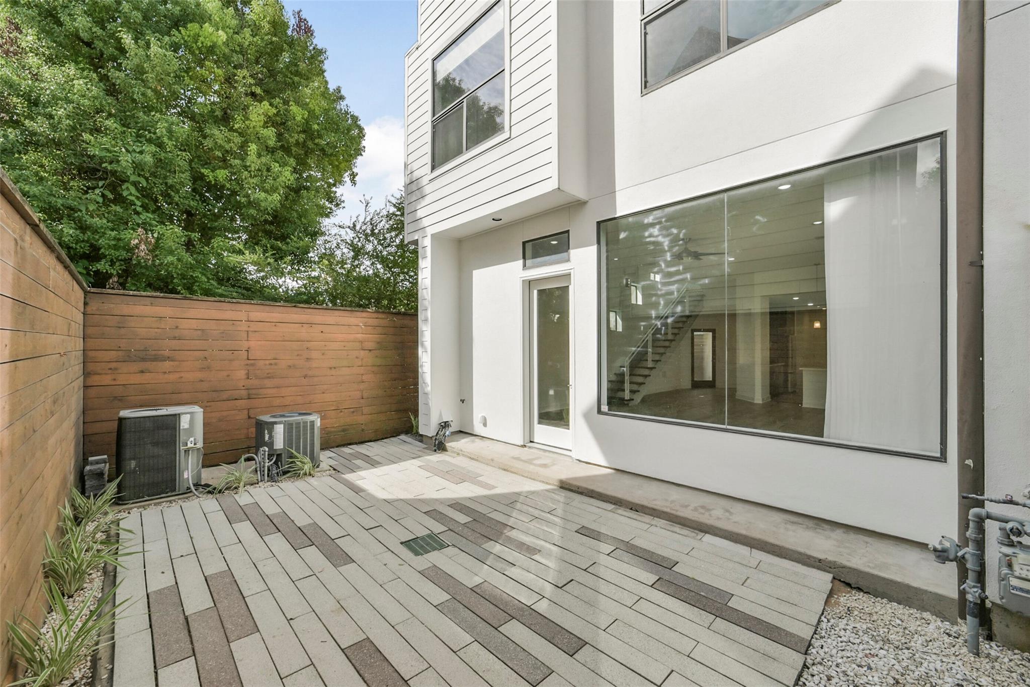 Modern townhouse patio with patterned pavers, a wooden privacy fence, and large windows.