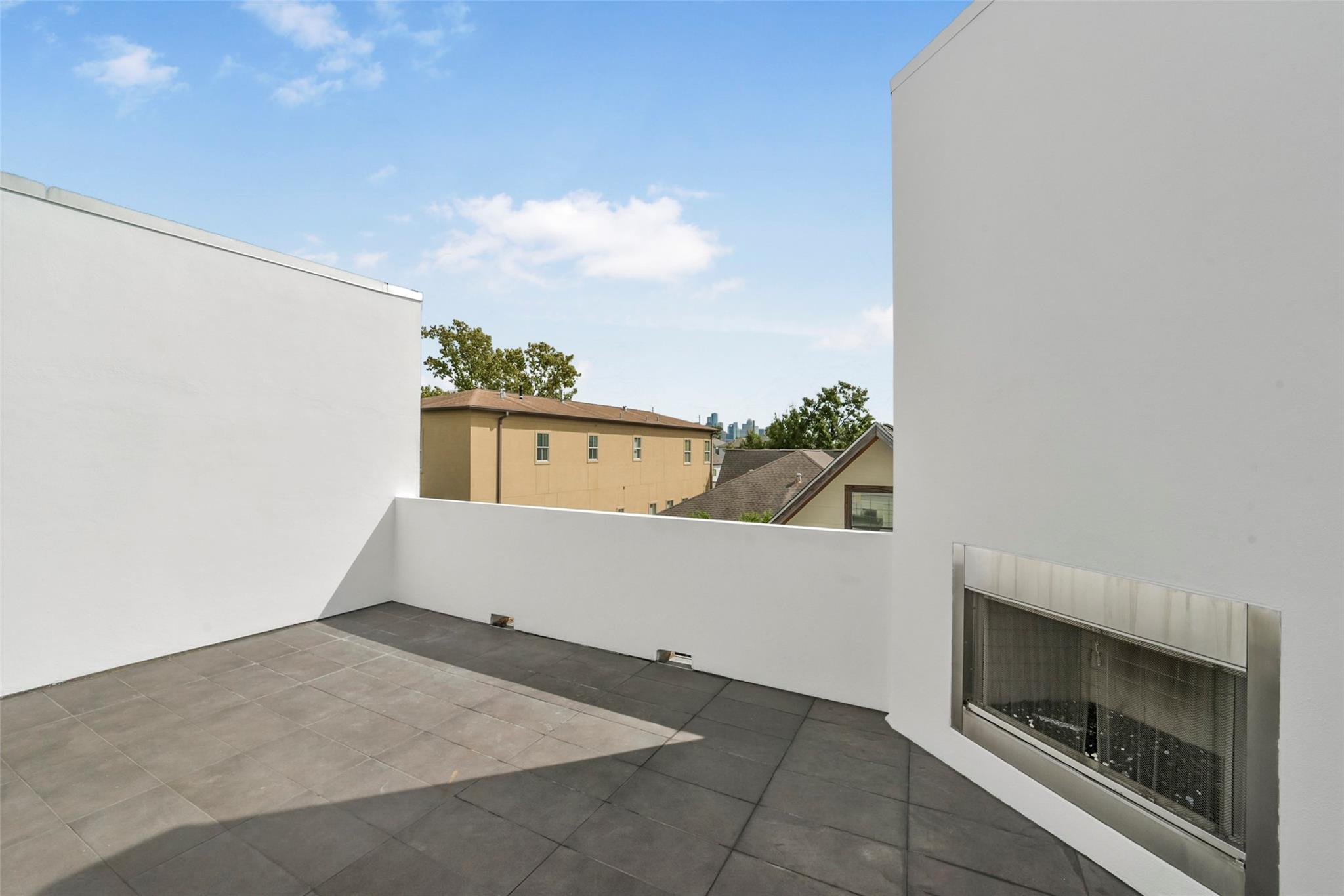 Rooftop terrace with gray tile flooring, built-in fireplace, and distant city skyline.