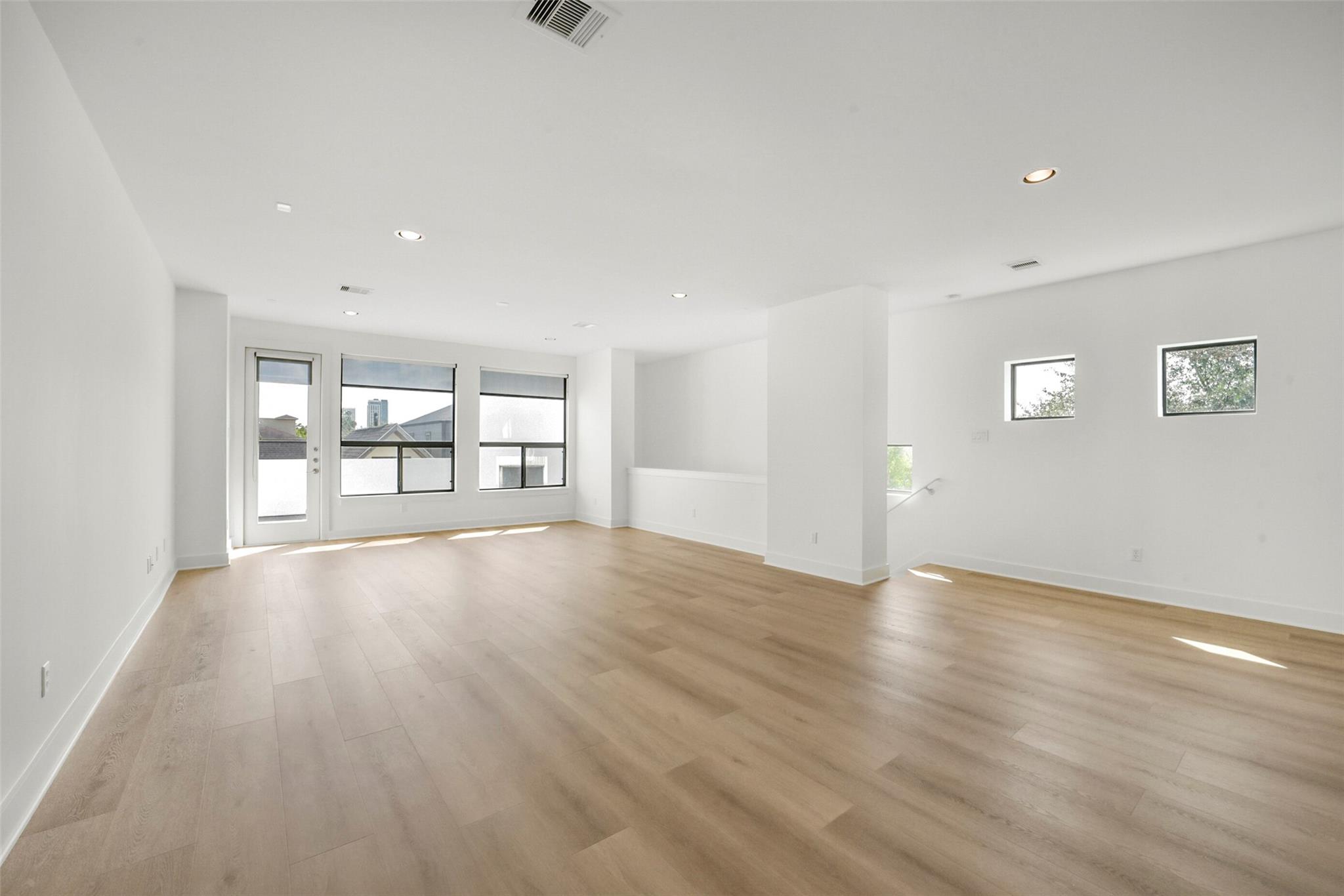 Vacant living area with light wood floors, large windows, and a glass door.
