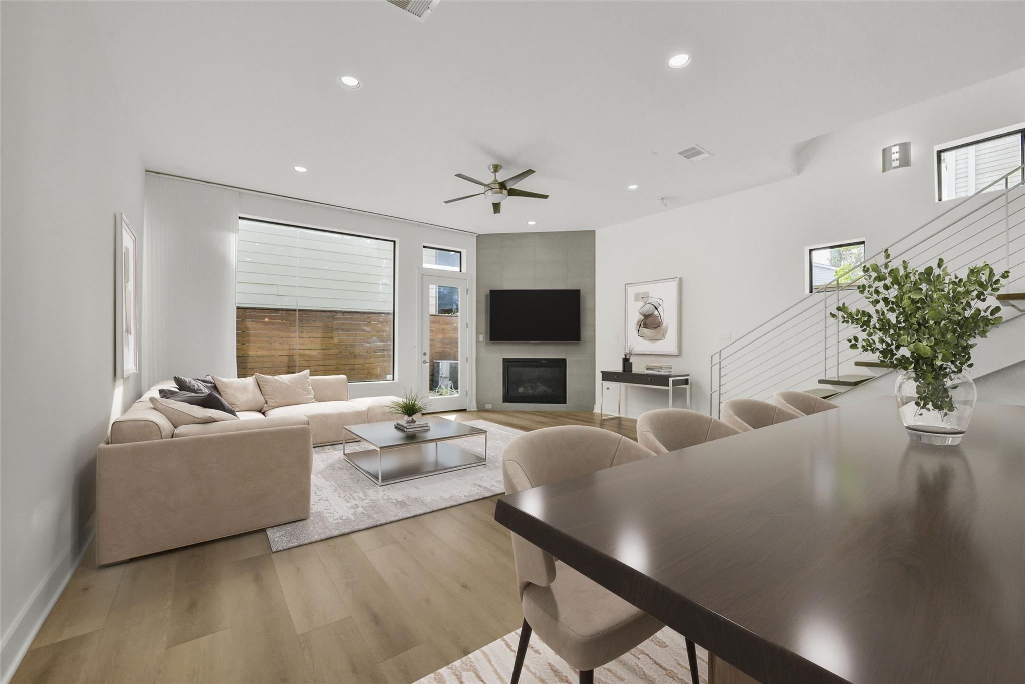 Staged living room with a beige sectional, fireplace, and staircase beside the dining area.