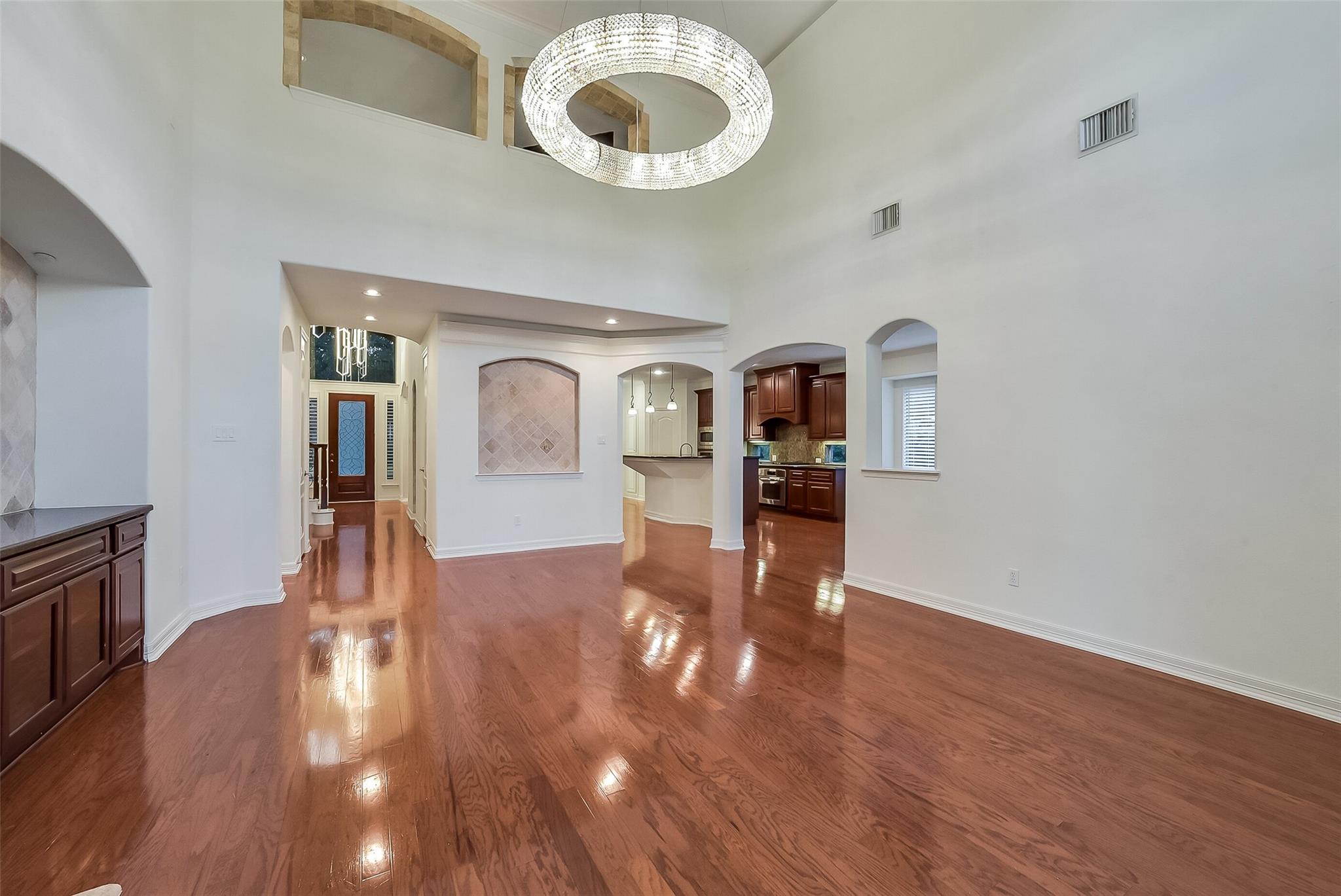 Unfurnished dining area with glossy hardwood floors, a circular chandelier, and arched openings to the kitchen.
