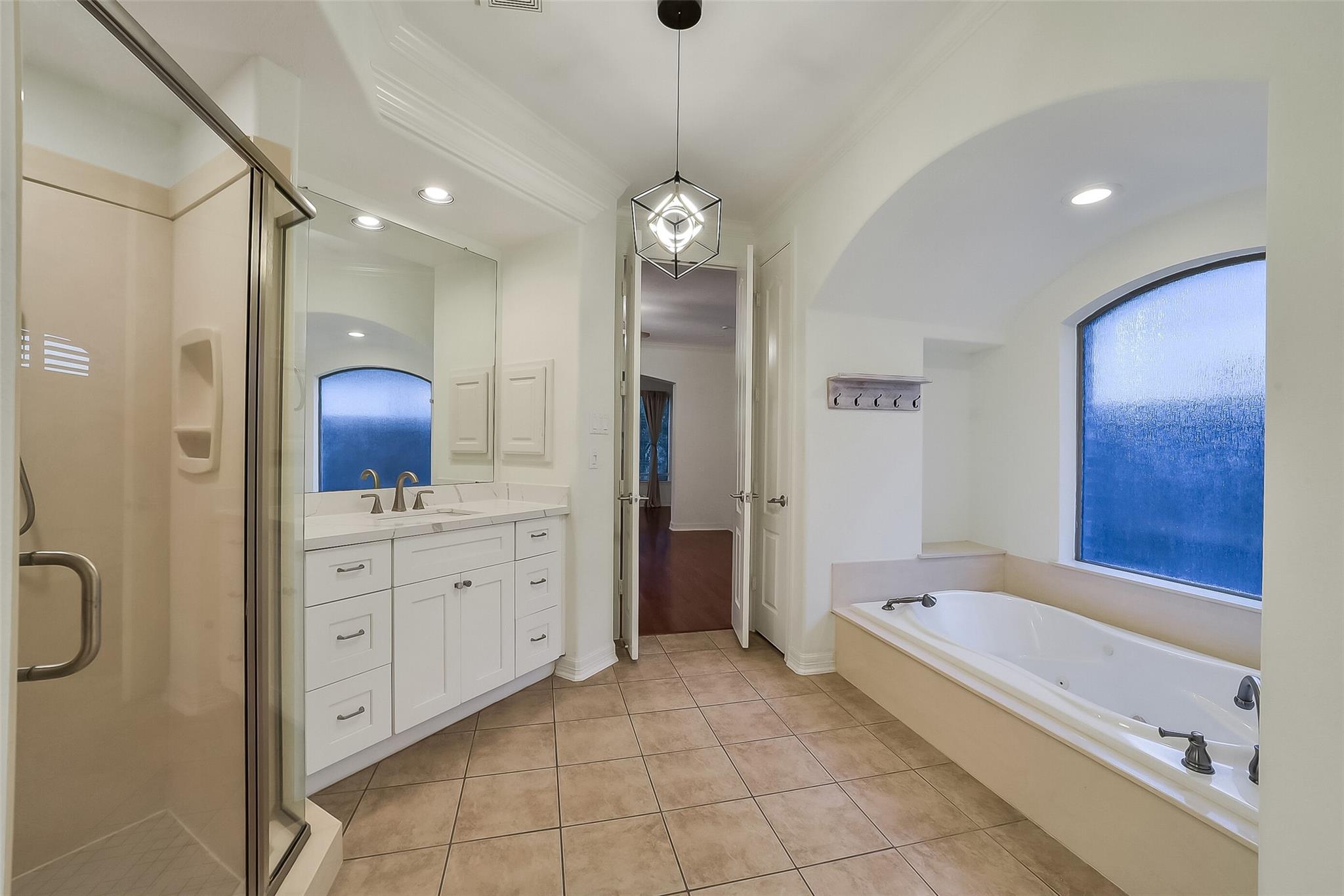 Bathroom with a glass shower, white double vanity, and soaking tub beneath an arched blue window.