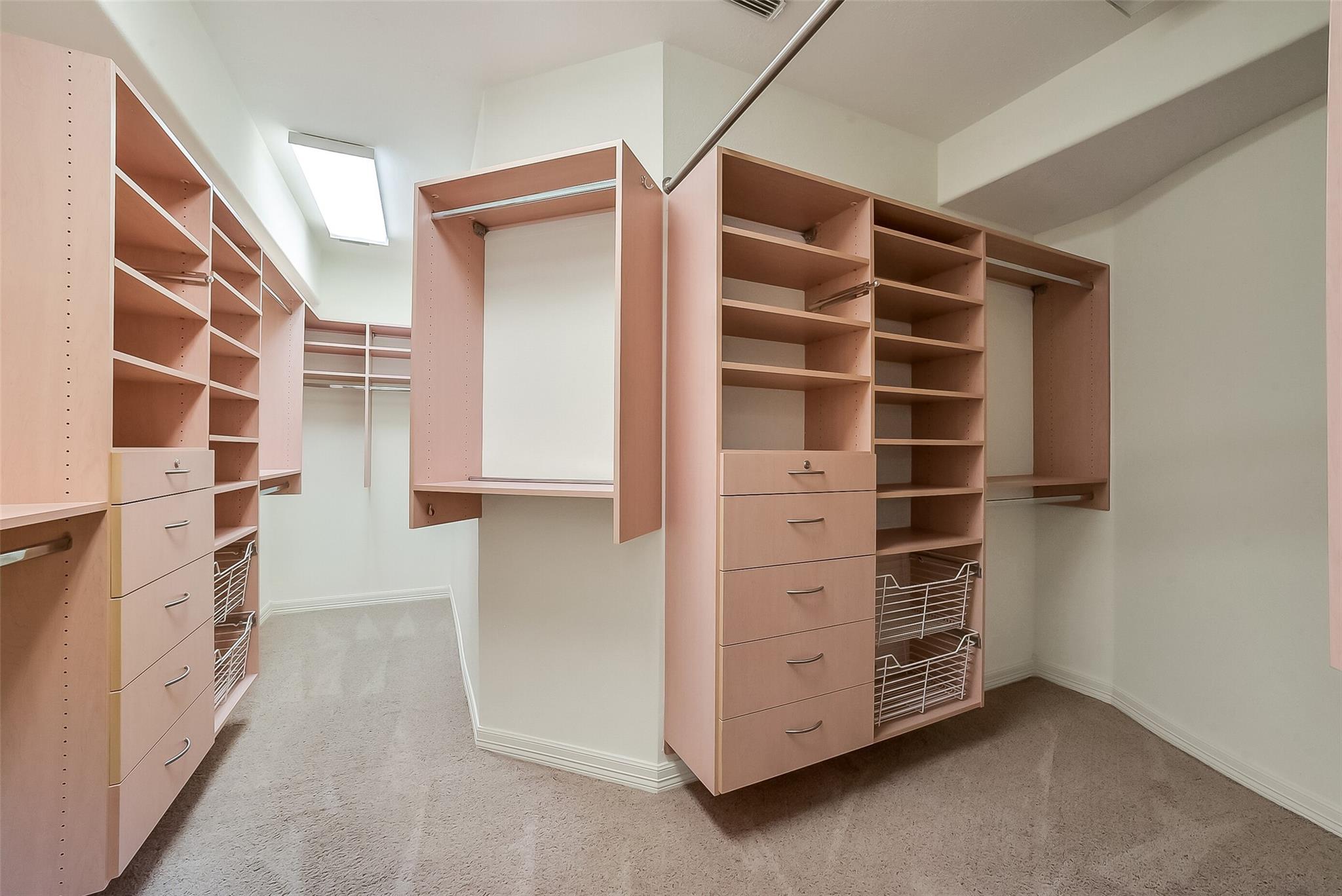 Walk-in closet with extensive built-in shelving, drawers, wire baskets, and a skylight.