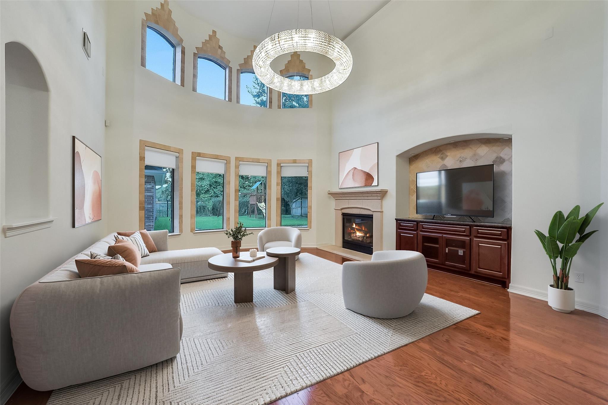 Vaulted living room with tall windows, a lit fireplace, and a television above dark wood cabinets.